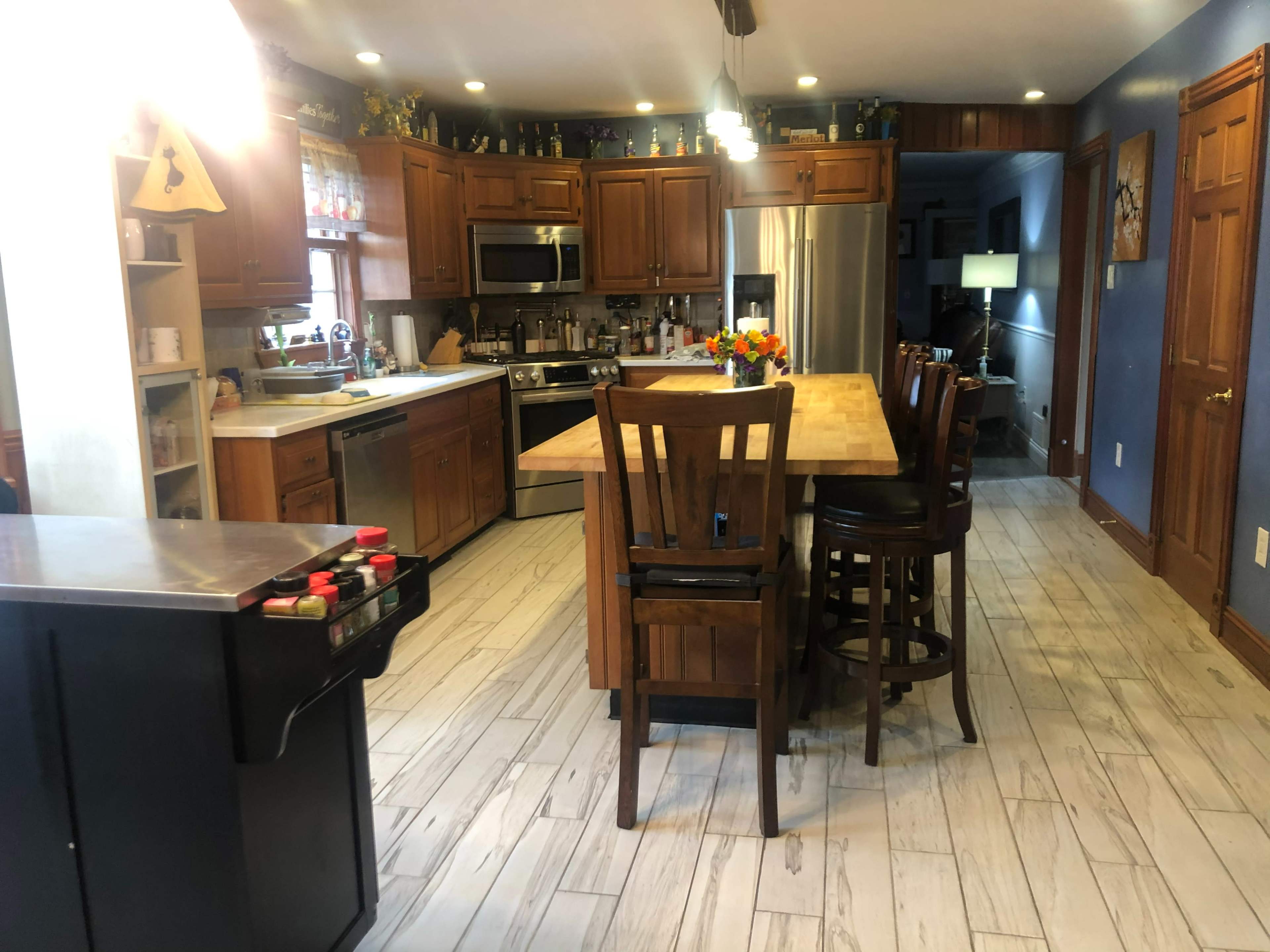A spacious kitchen with wooden cabinets, an island with seating, stainless steel appliances, and a tile floor.