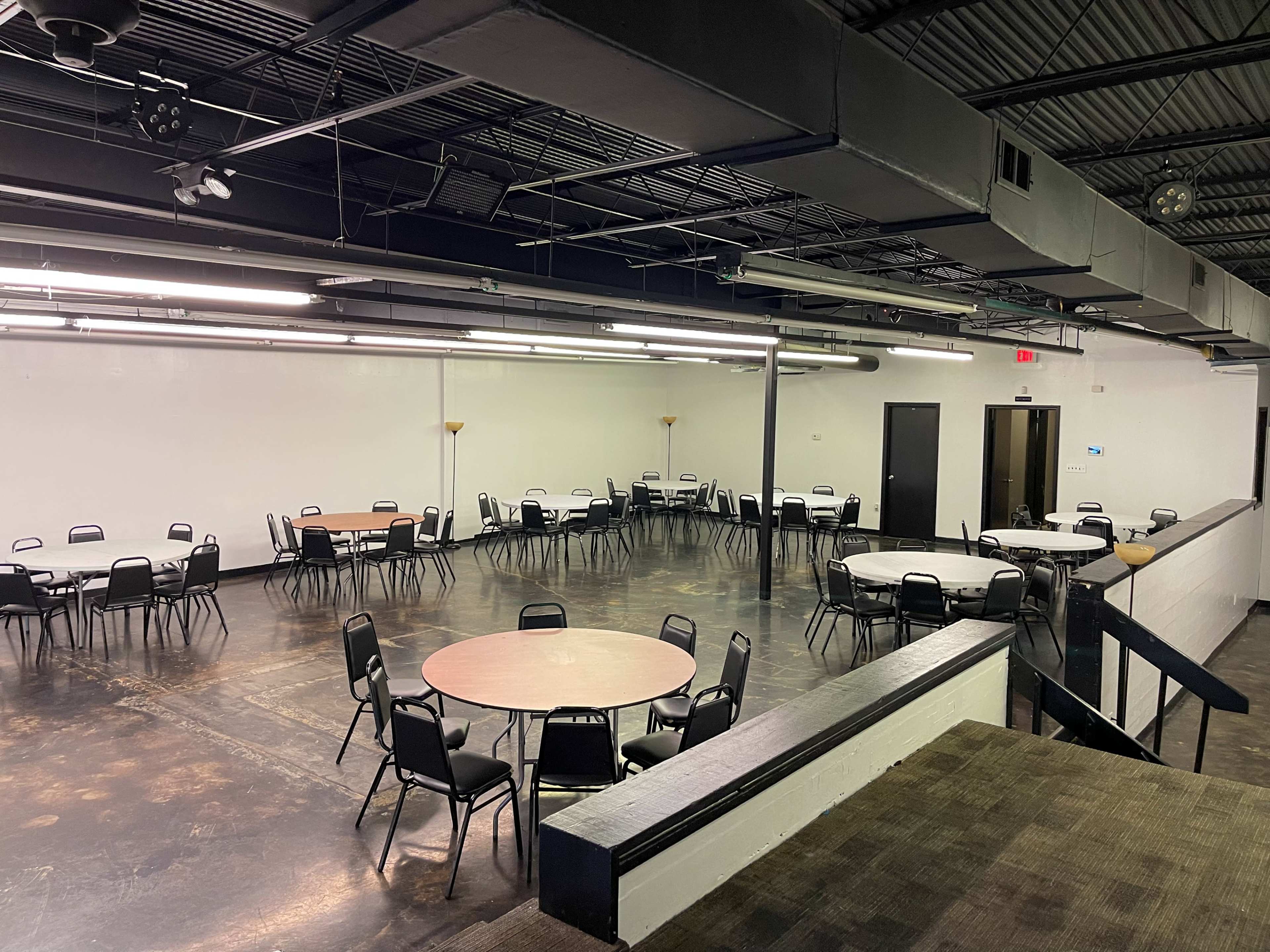 A spacious, empty hall with several round tables and chairs arranged throughout.