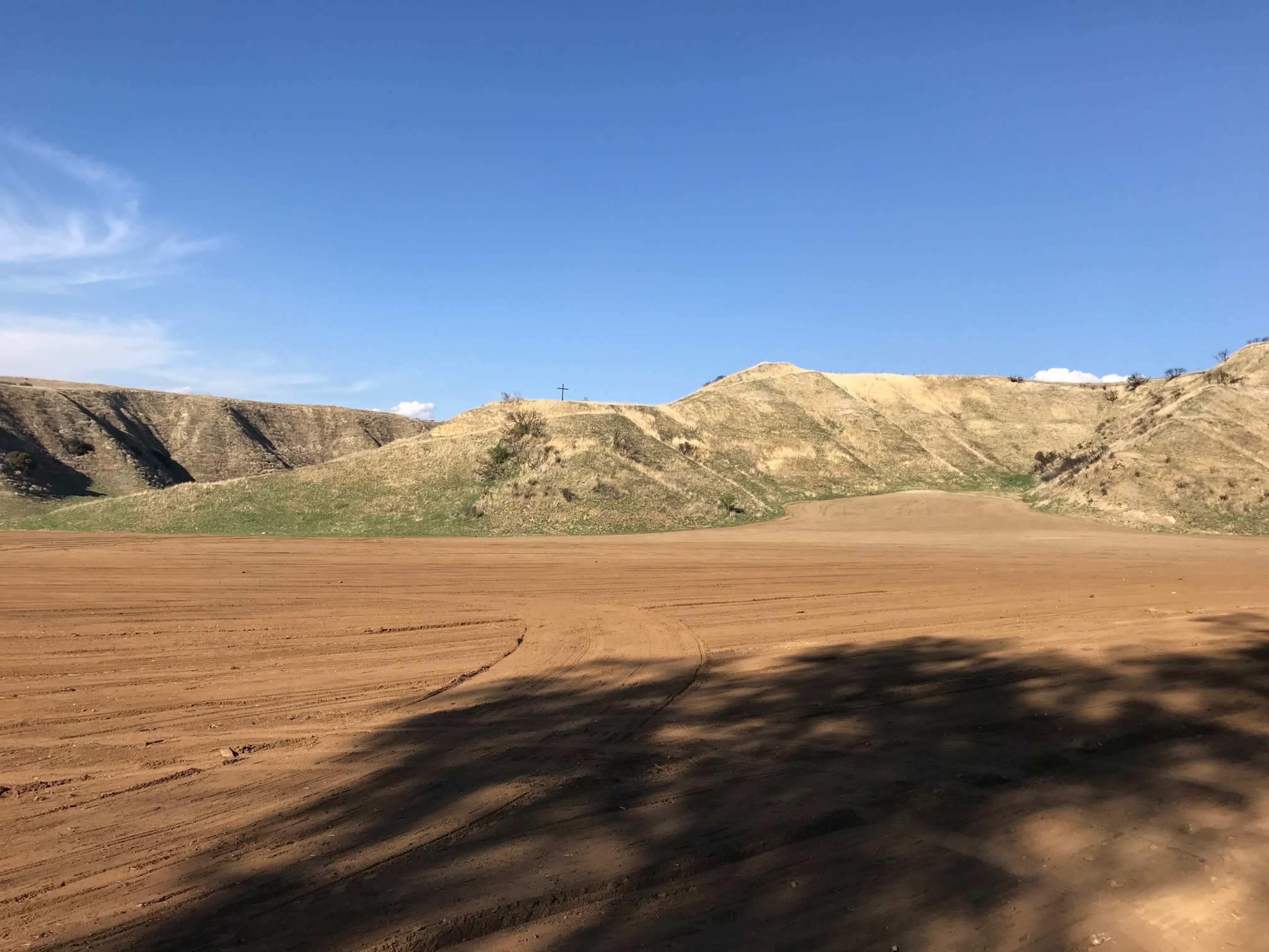 A flat, bare landscape stretches out with rolling hills in the background under a clear blue sky.