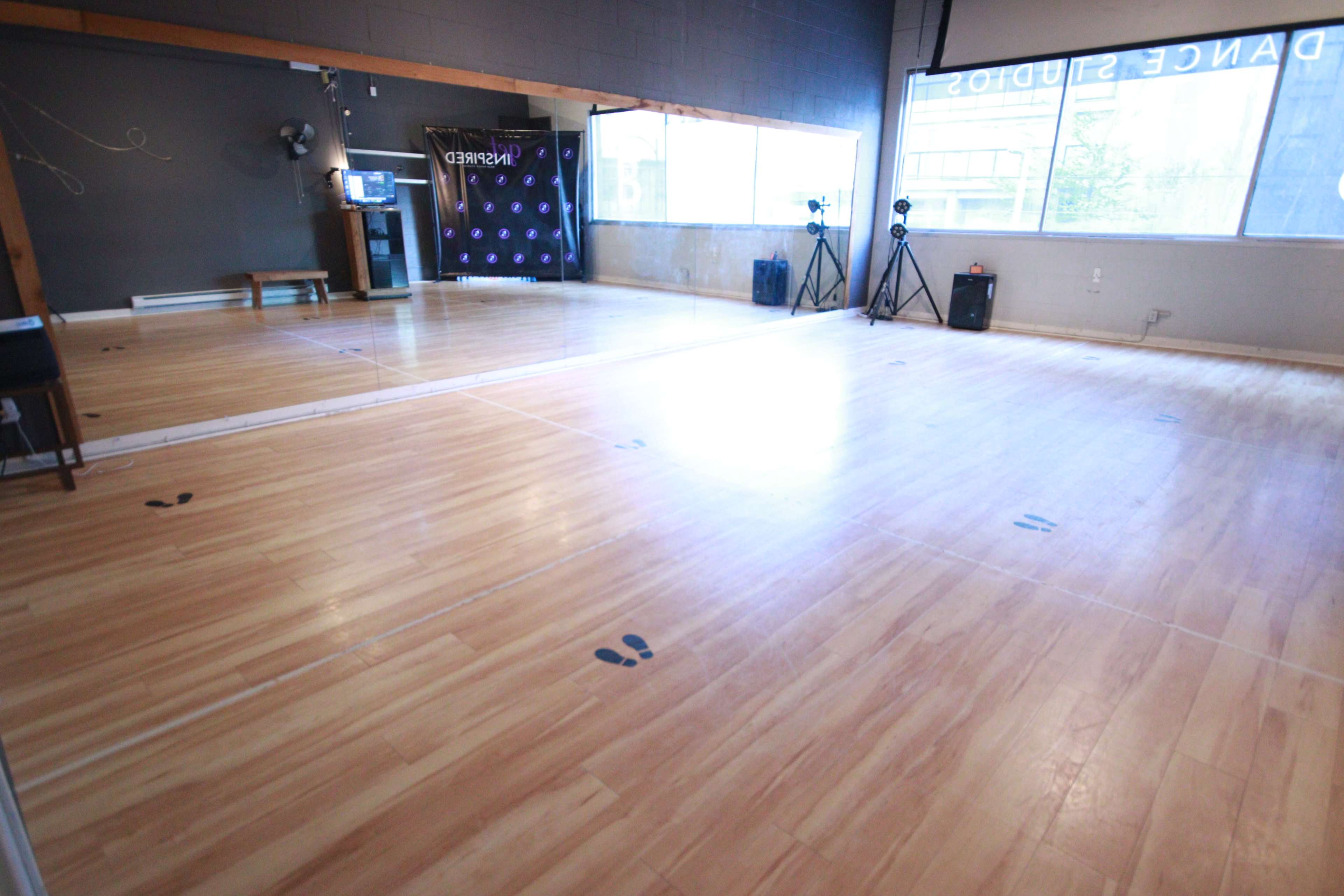 An empty dance studio features a wooden floor with marked footprints, a wall mirror, and a backdrop displaying the words "Dance Studio."