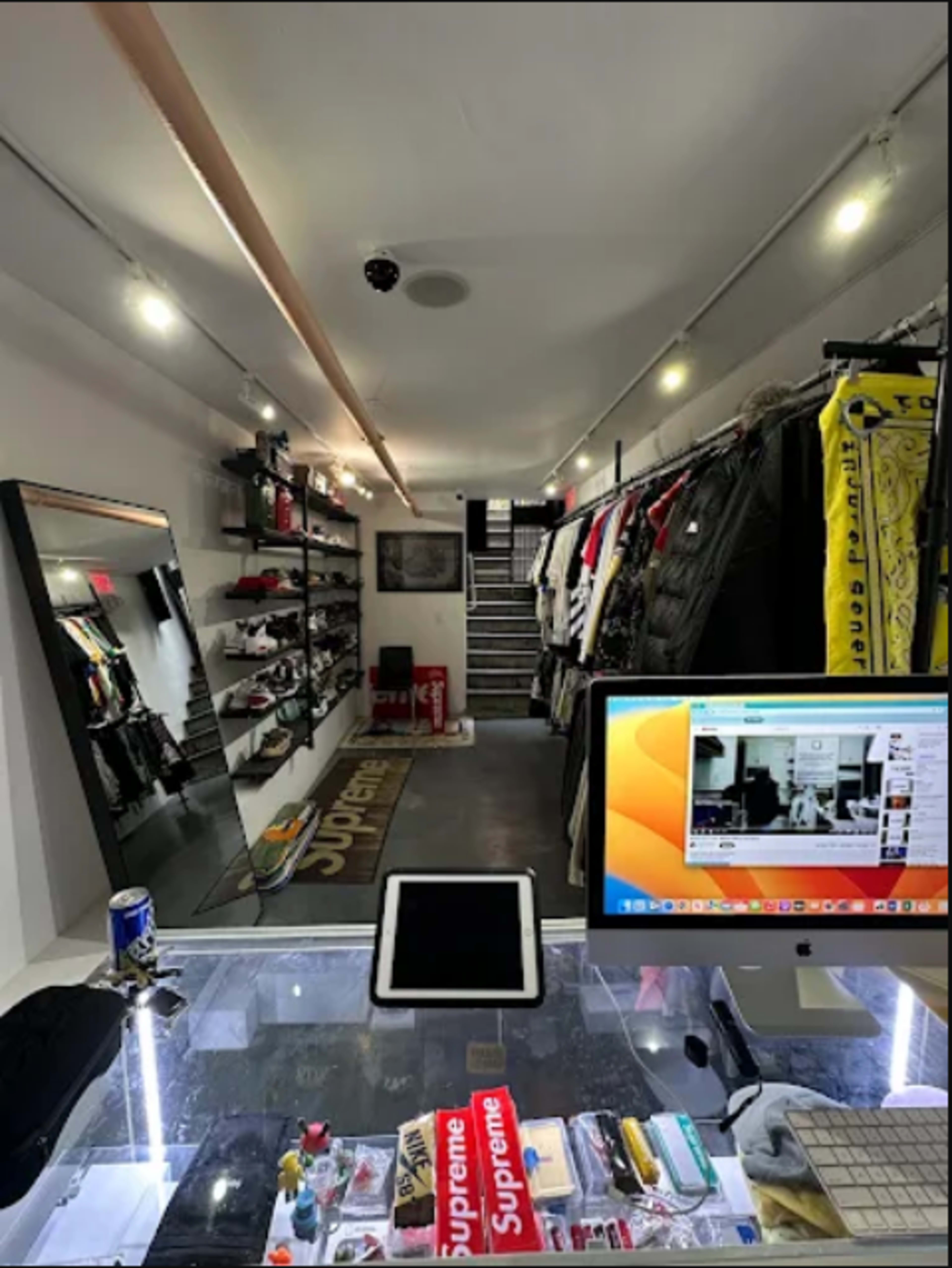 The image shows a retail store interior displaying clothing and accessories on shelves, with a checkout area featuring electronic devices and merchandise.