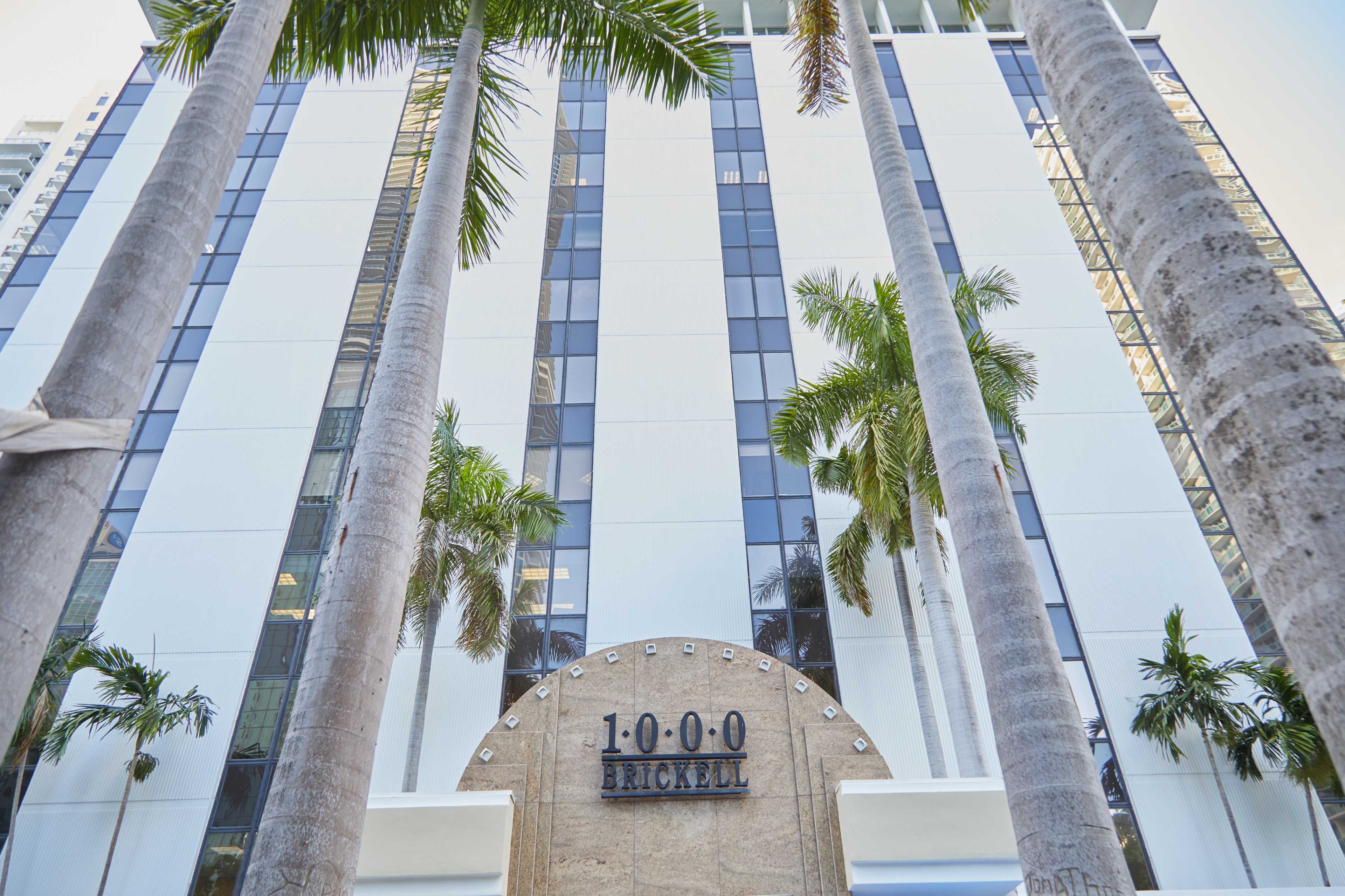The image shows a modern building titled "1000 Brickell" with tall palm trees in the foreground.