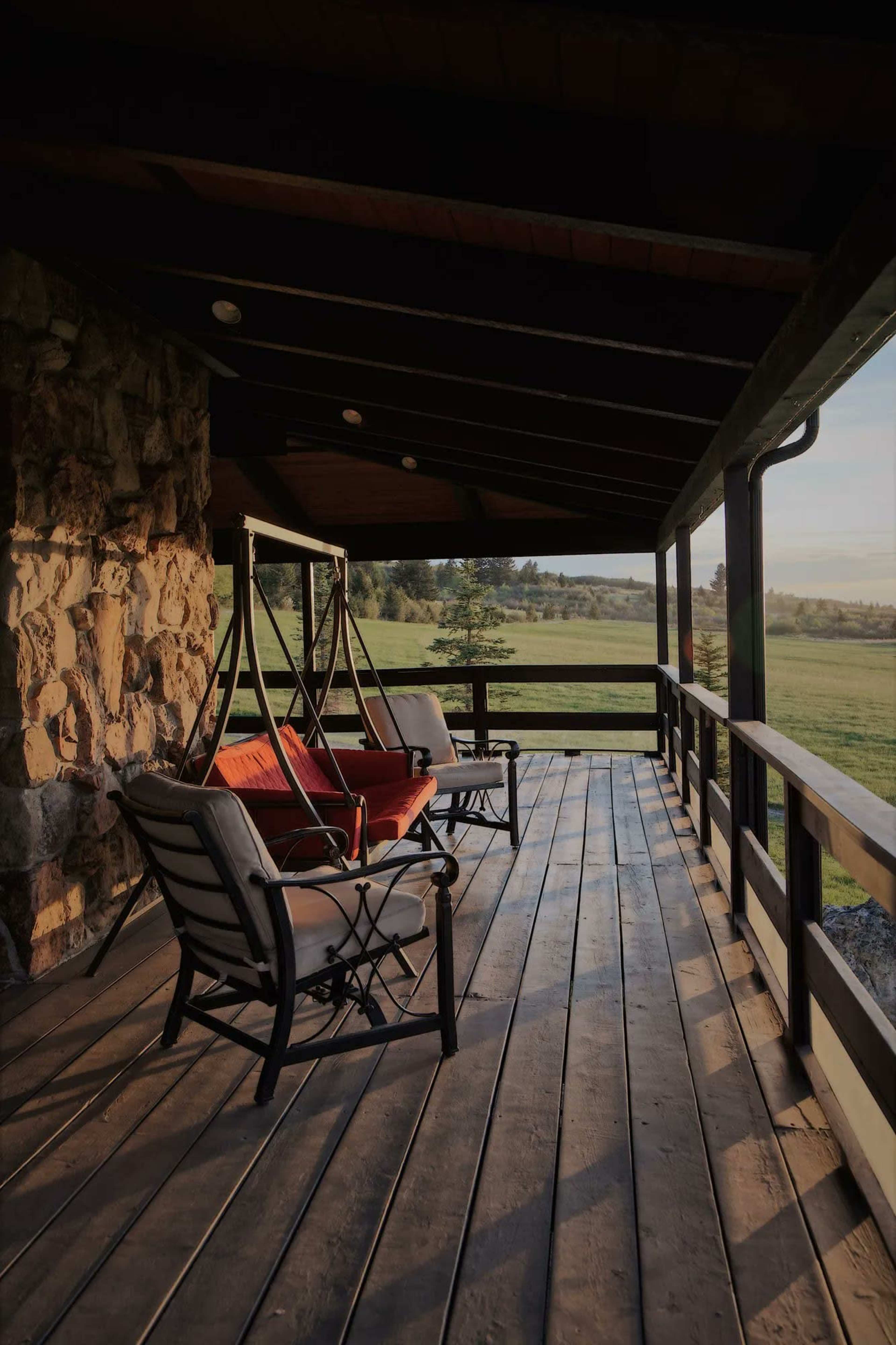 The image shows a wooden porch with two swings and two chairs, overlooking a grassy field.