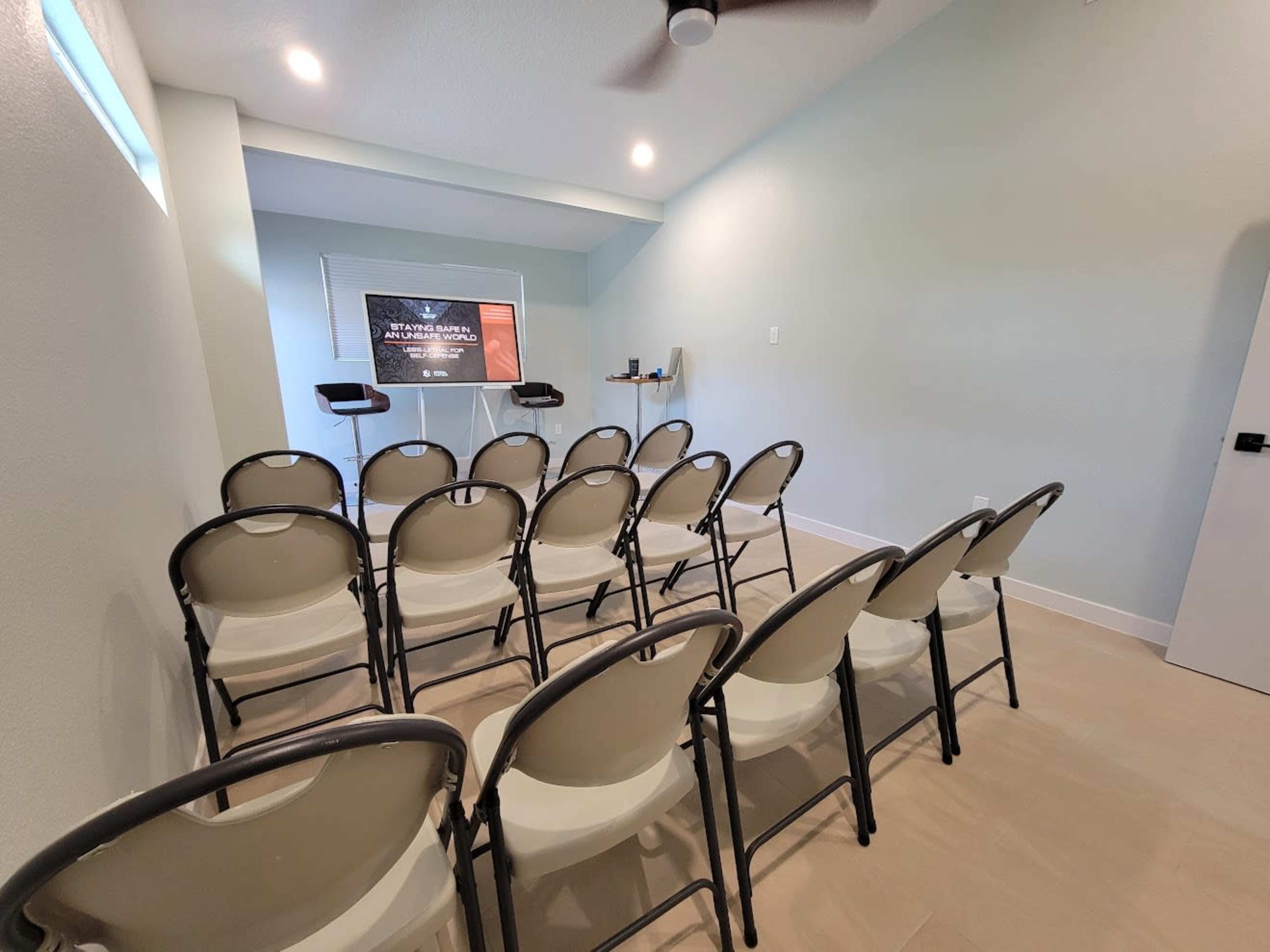 The image shows a small meeting room with several rows of folding chairs facing a presentation screen.