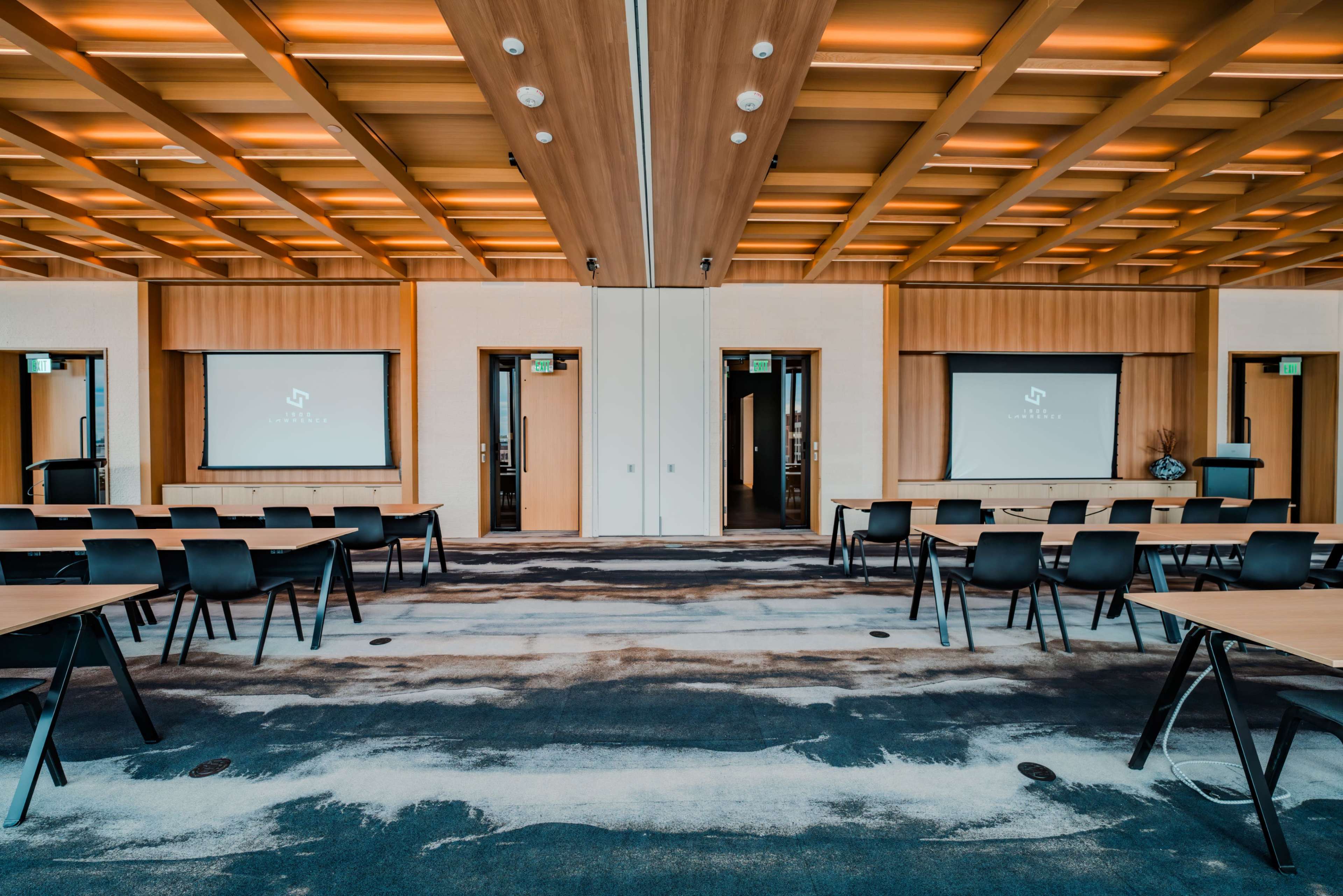 A conference room with multiple seating arrangements and projection screens at the front, featuring wooden paneling and a modern design.