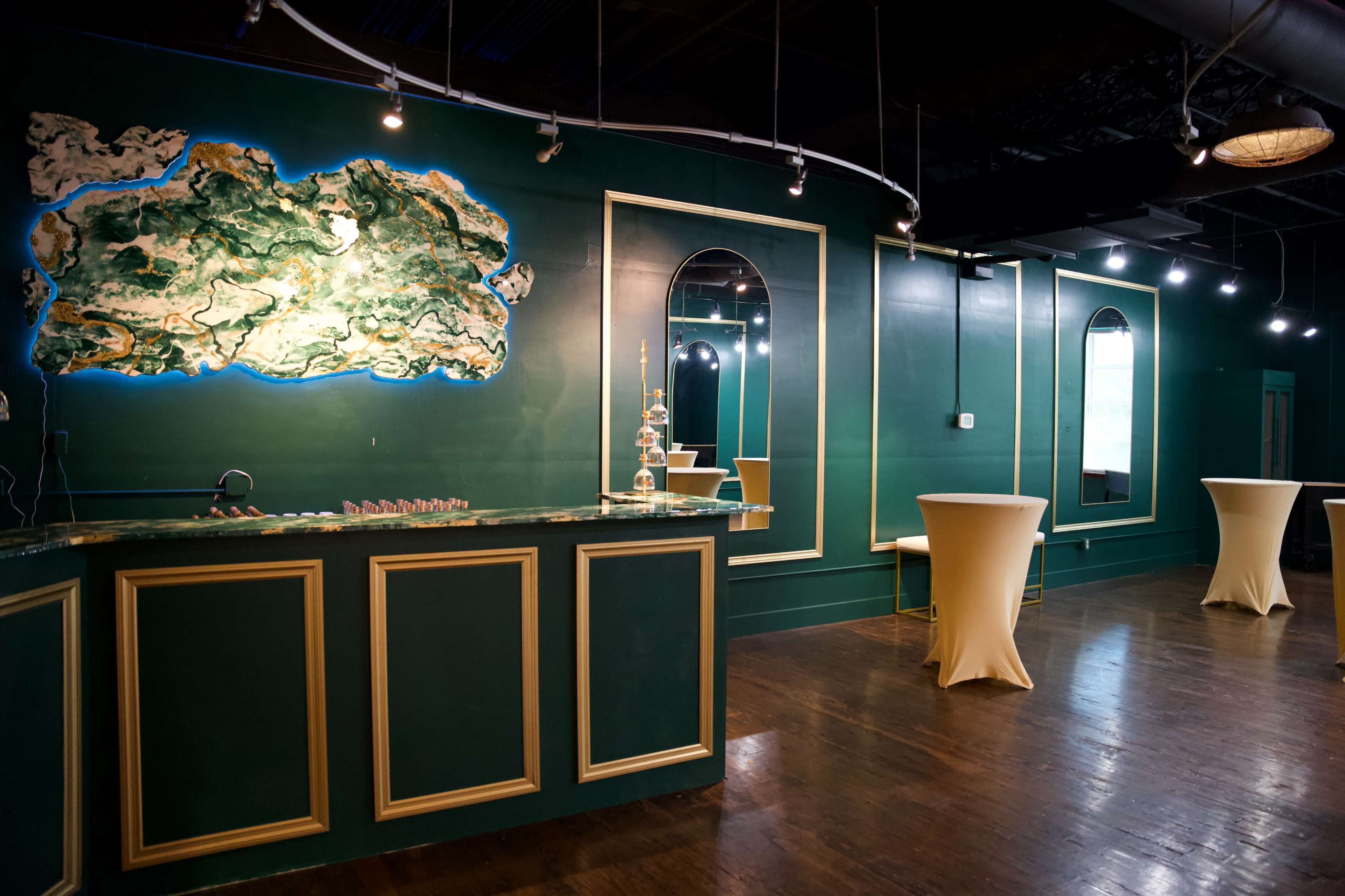 The interior of a bar features a green wall with a large decorative map, a mirrored wall, and several tall tables.