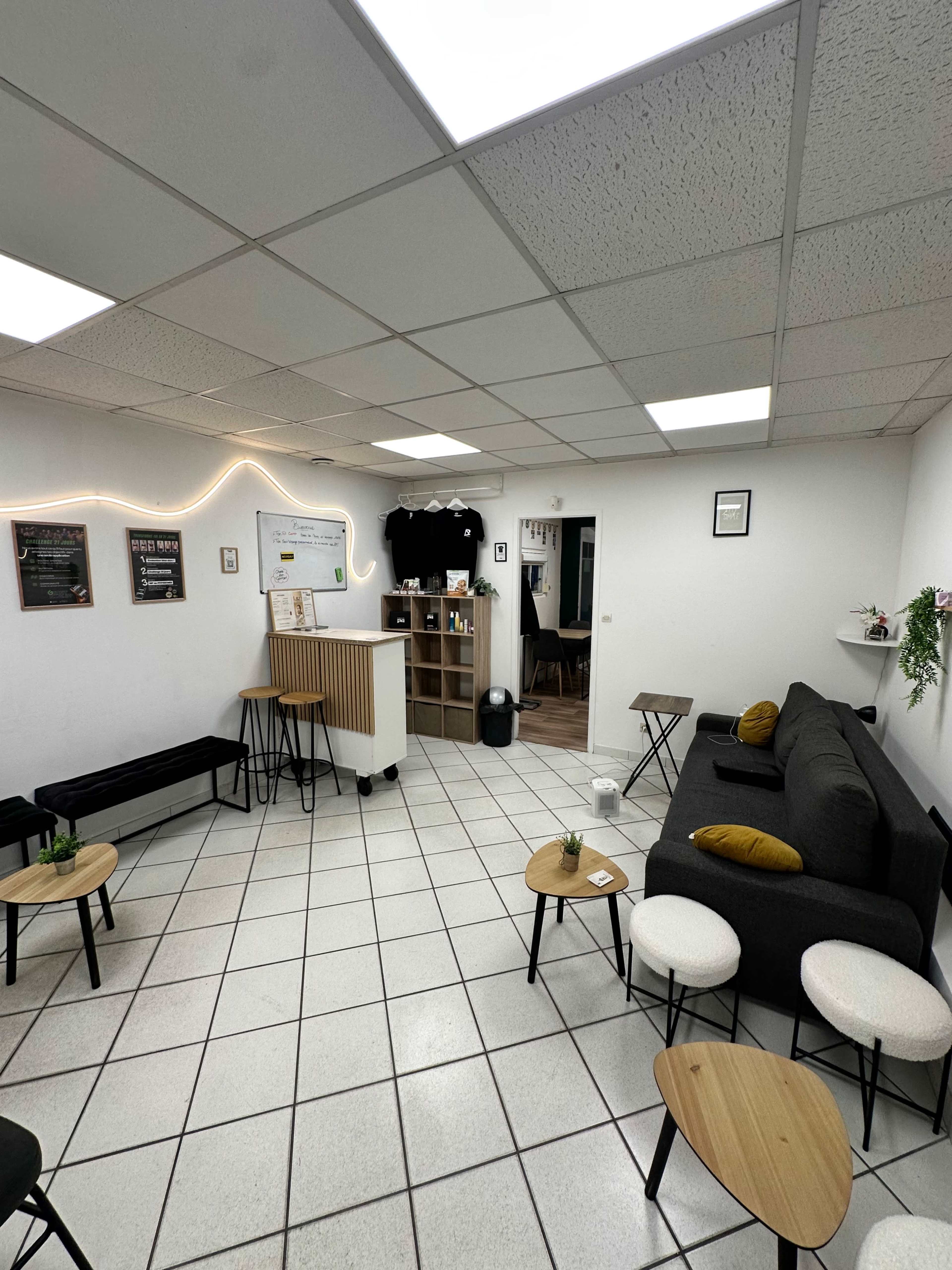 The image shows a clean, open room with a seating area featuring a gray sofa, small wooden tables, and a counter against one wall.