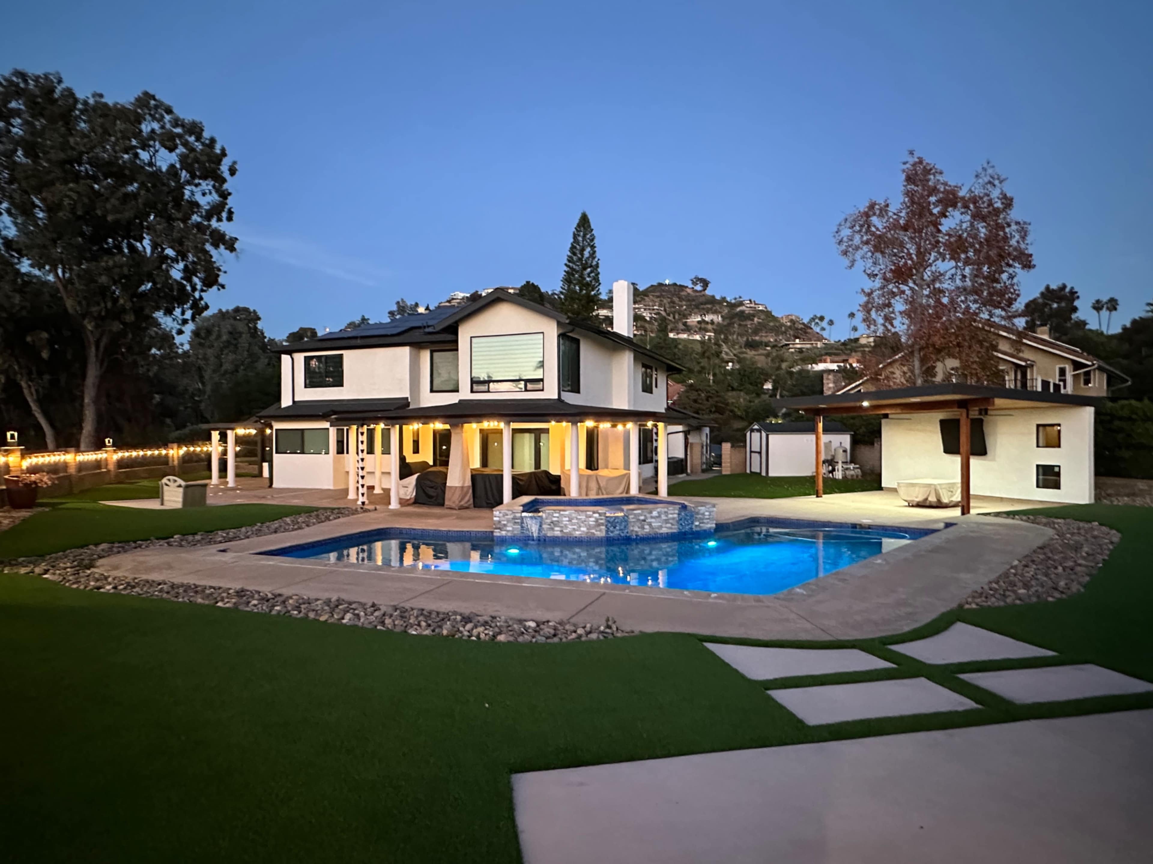 A two-story house with a pool surrounded by a landscaped yard at twilight.
