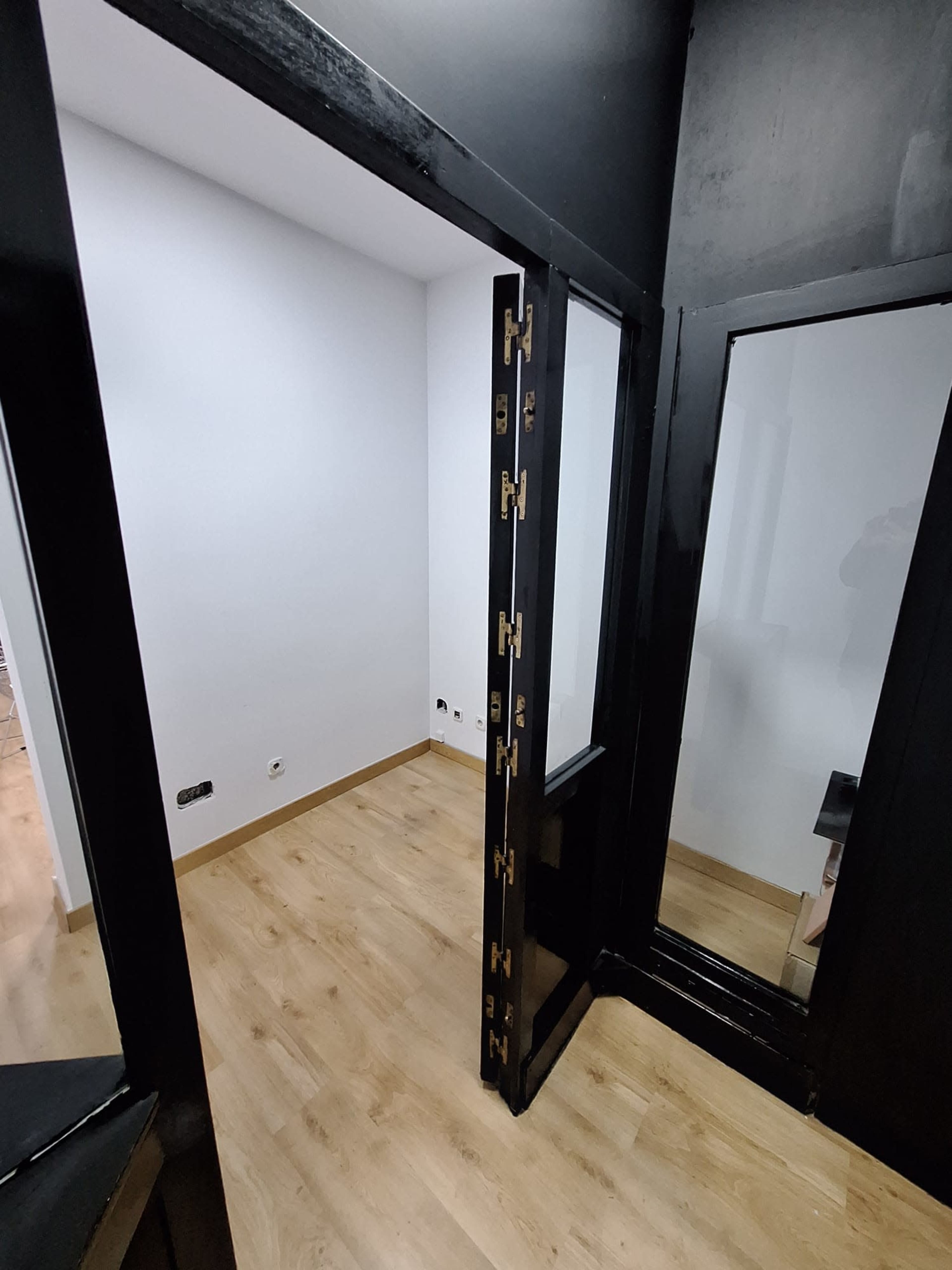 The image shows a small, partially enclosed room with black walls, a wooden floor, and a central black pillar featuring decorative elements.