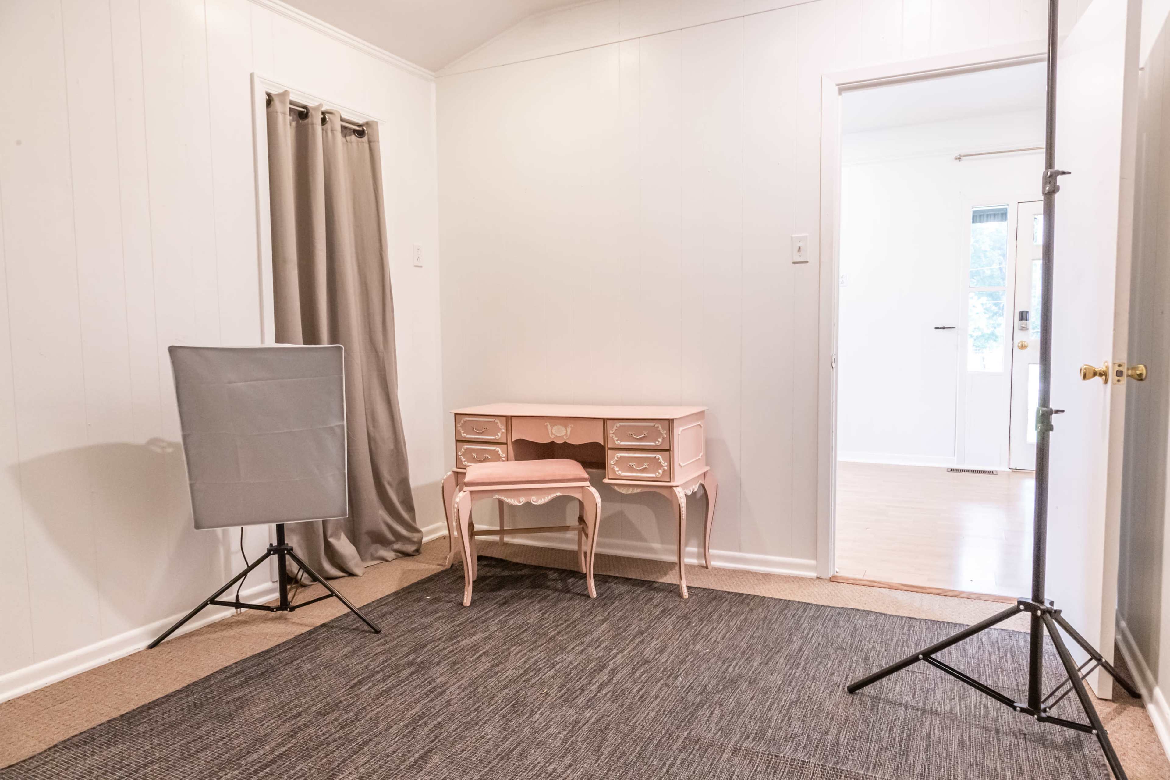 A small room with a pink desk and matching chair, a gray backdrop setup, and a door leading to another area.