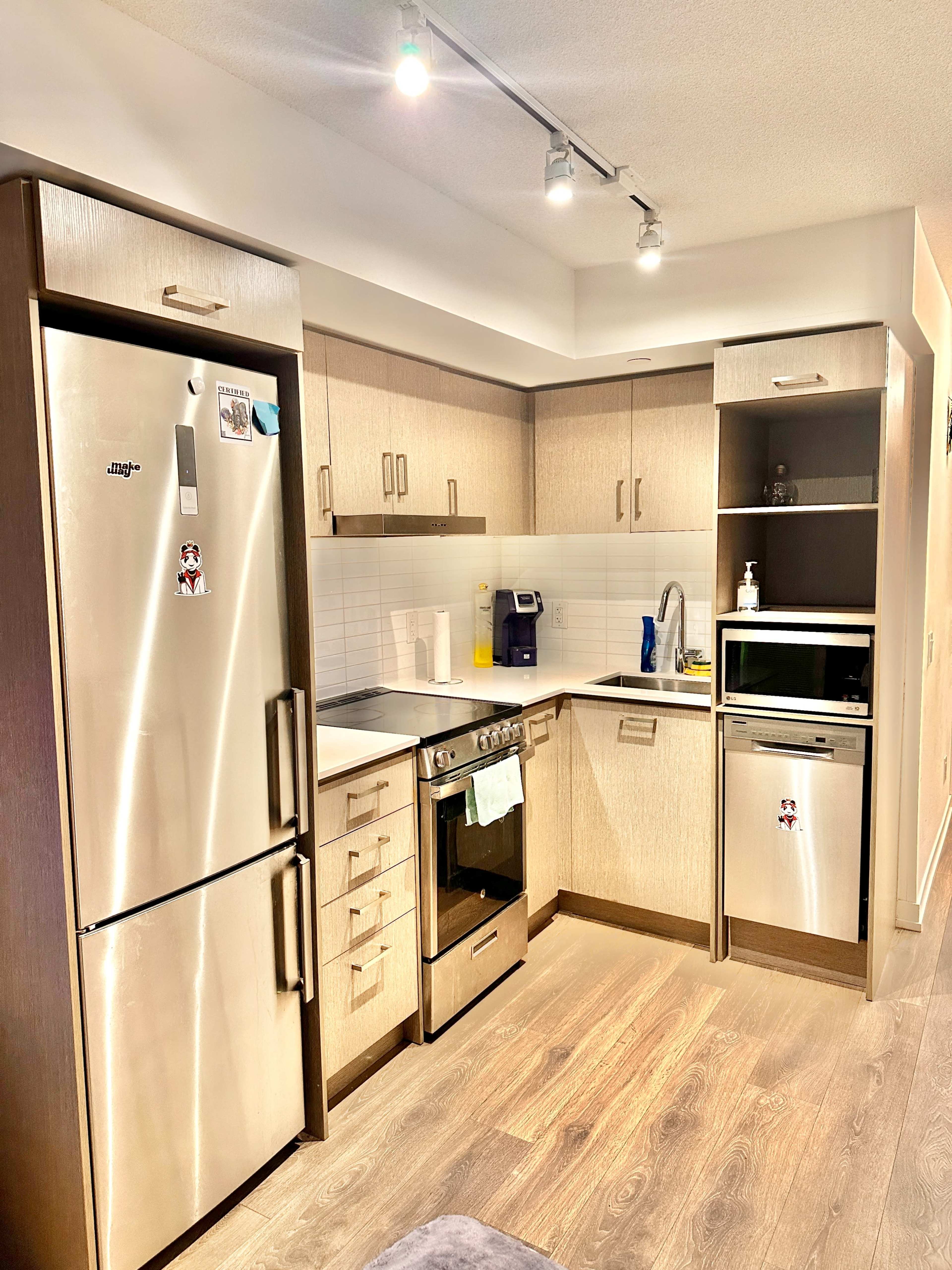 The image shows a modern kitchen with stainless steel appliances, light-colored cabinetry, and a compact layout.
