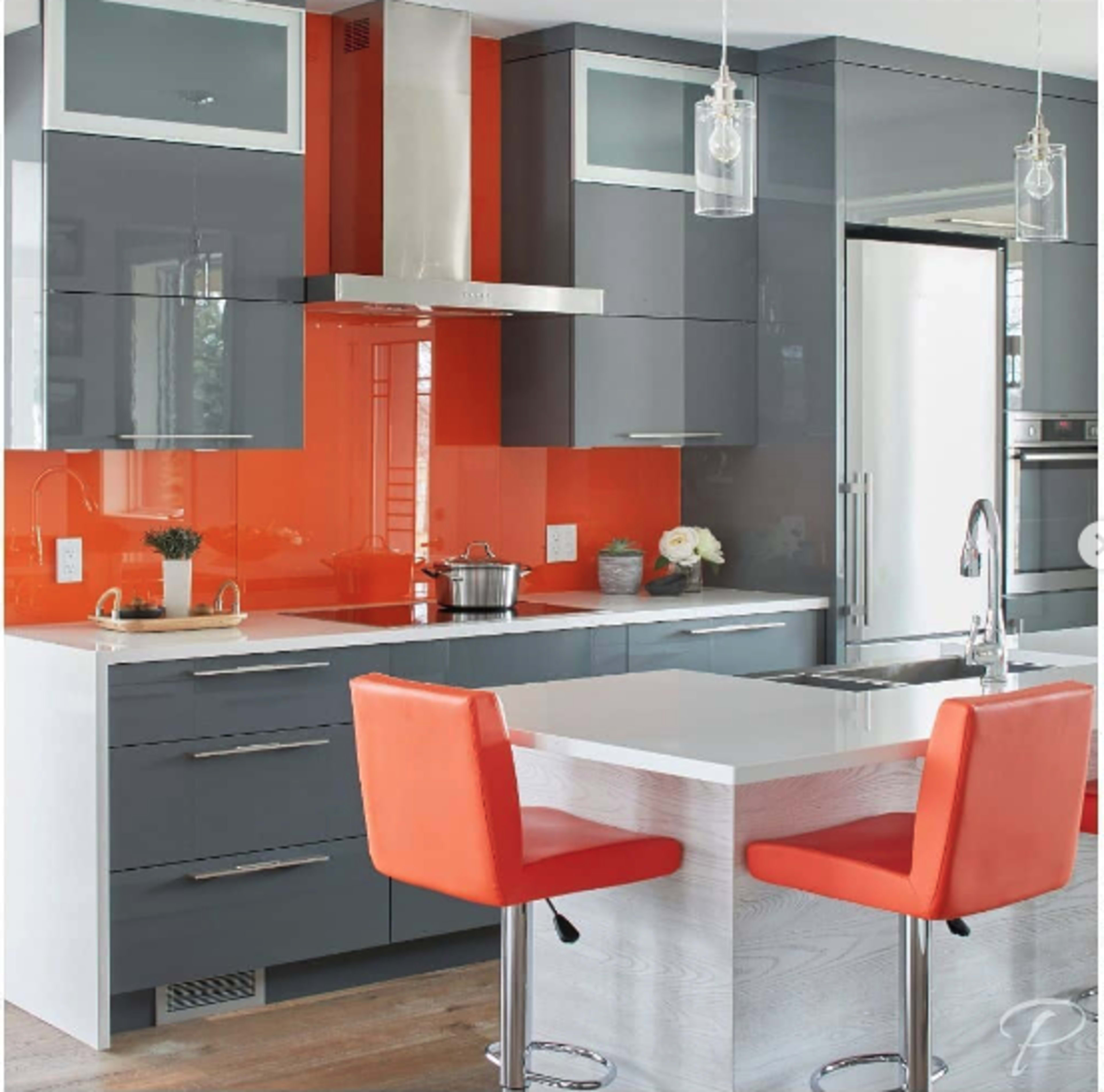 A modern kitchen featuring gray cabinets, an orange backsplash, and a central island with orange bar stools.