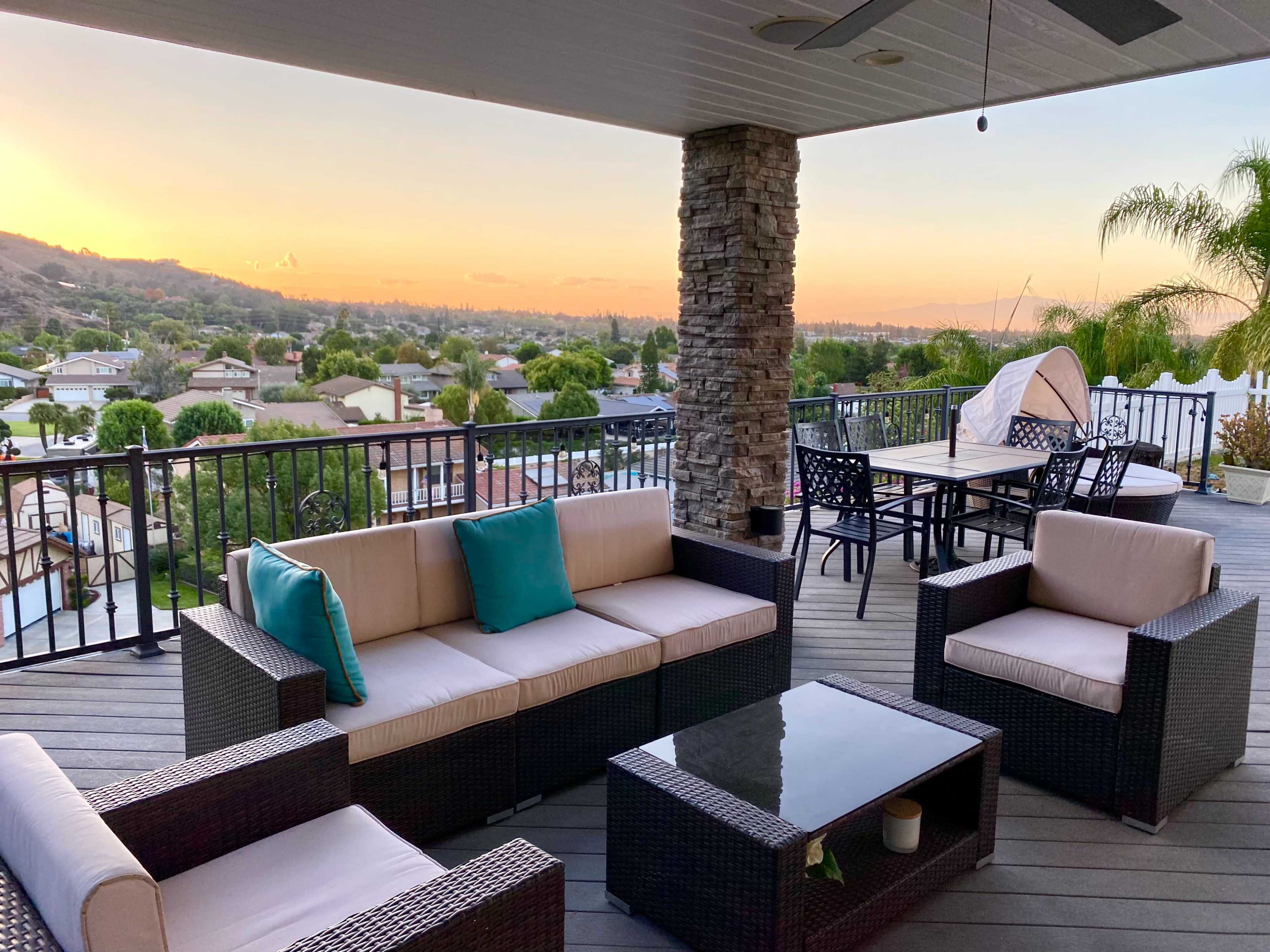 An outdoor patio area with seating, a table, and a view of a sunset over a suburban landscape.
