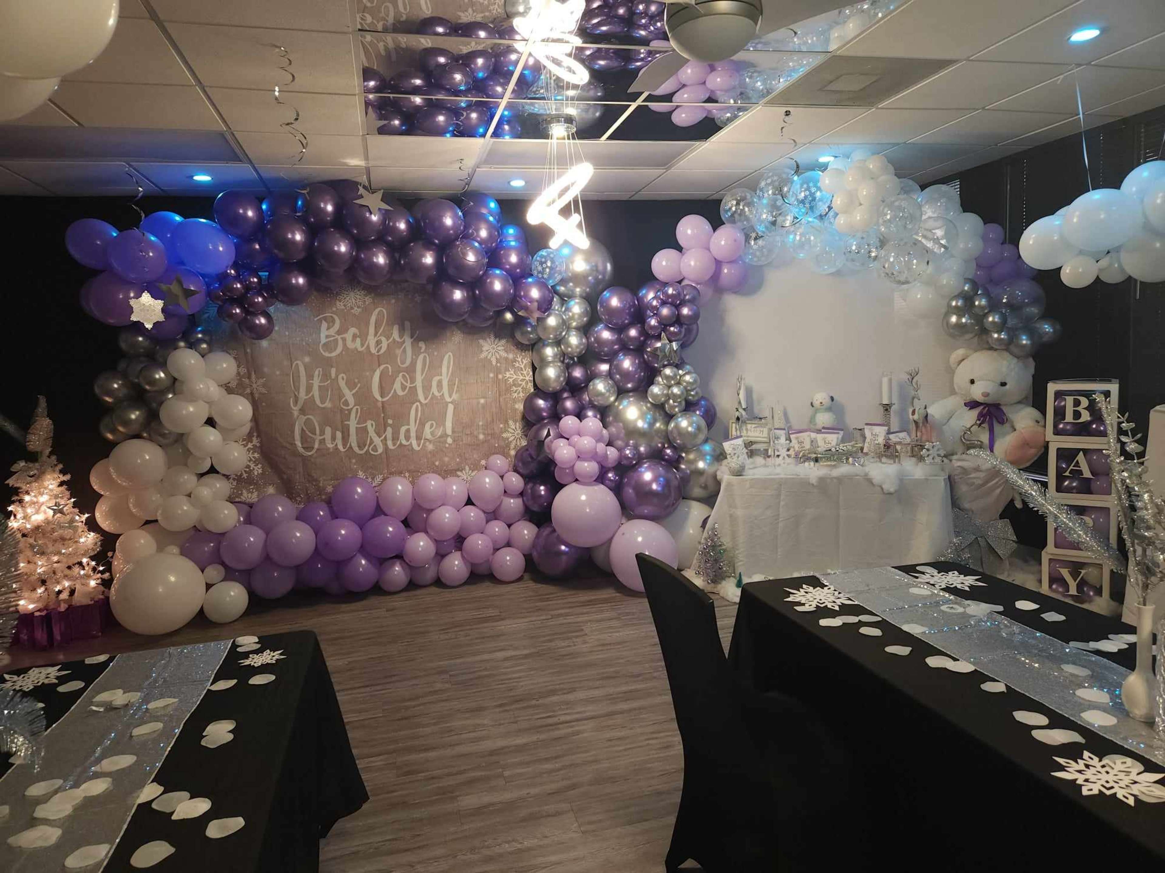 A decorated indoor space for a baby shower featuring balloon arches, a dessert table, and themed decorations.