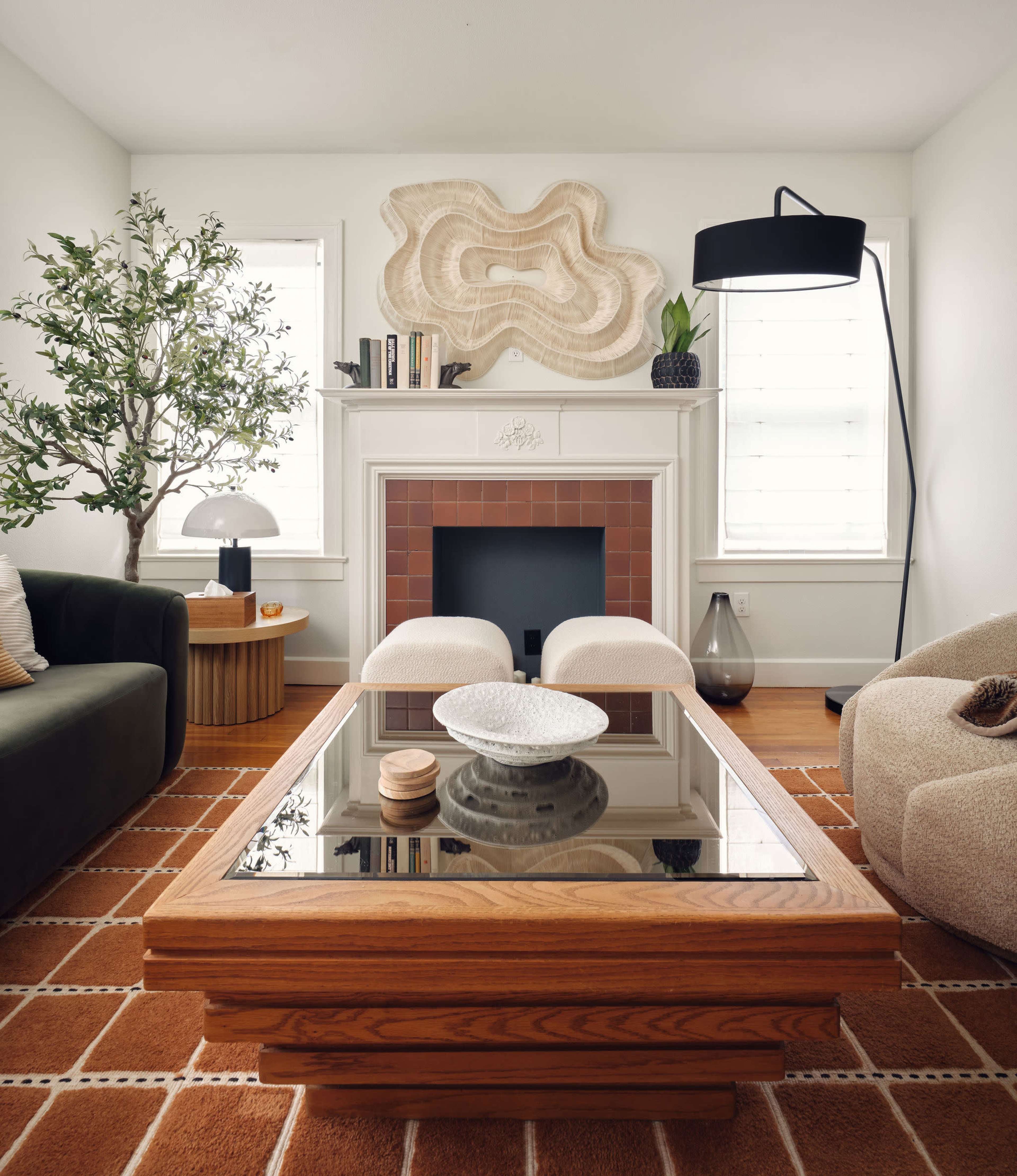 The living room features a coffee table with a mirrored top, surrounded by a dark green sofa and a light-colored armchair, with decorative elements like a lamp and a plant.