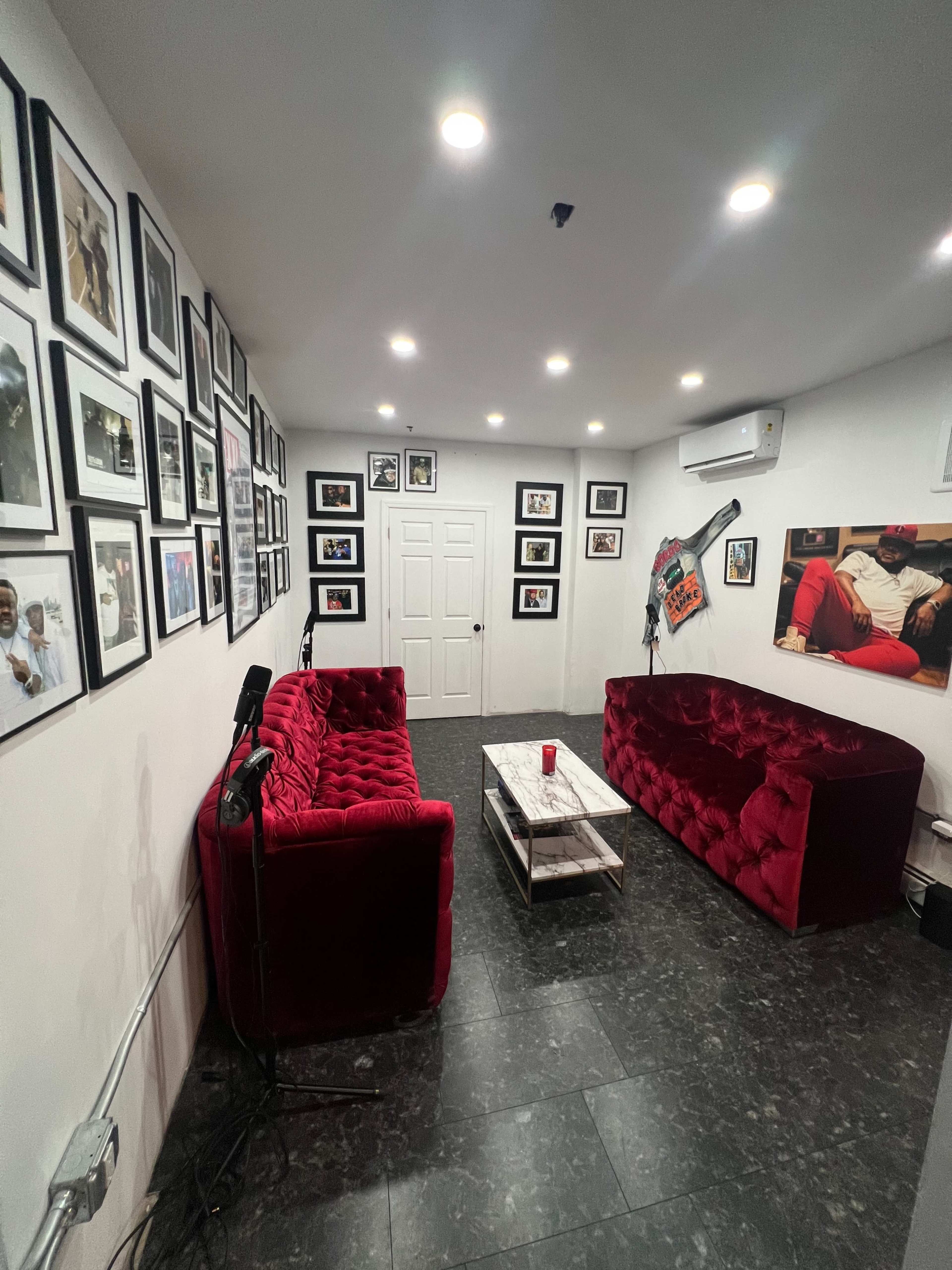 A room with two red velvet sofas facing a coffee table, surrounded by framed photographs on the walls.