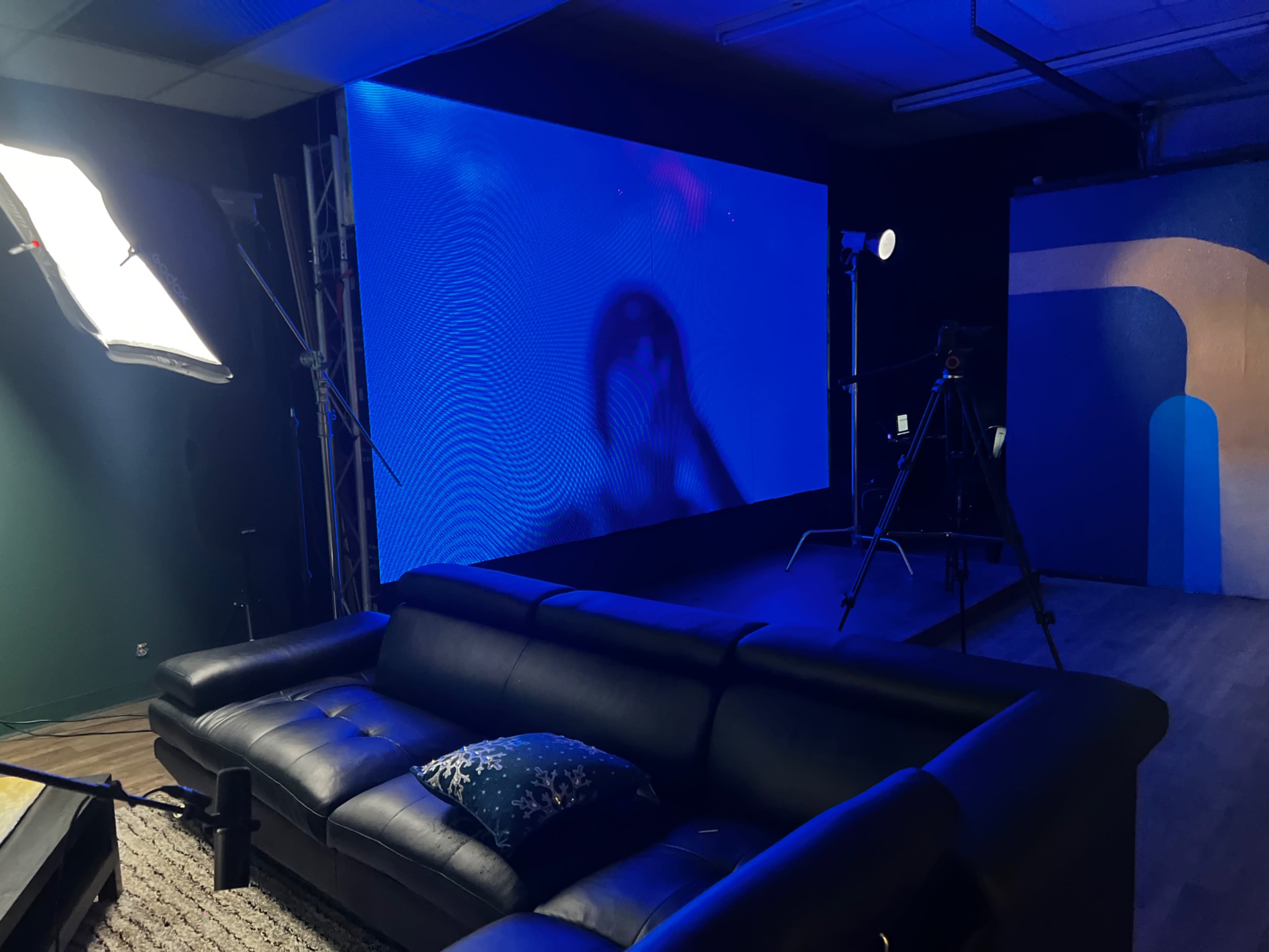 A dimly lit studio with a black couch, a large blue screen in the background, and several cameras and lights set up for a shoot.