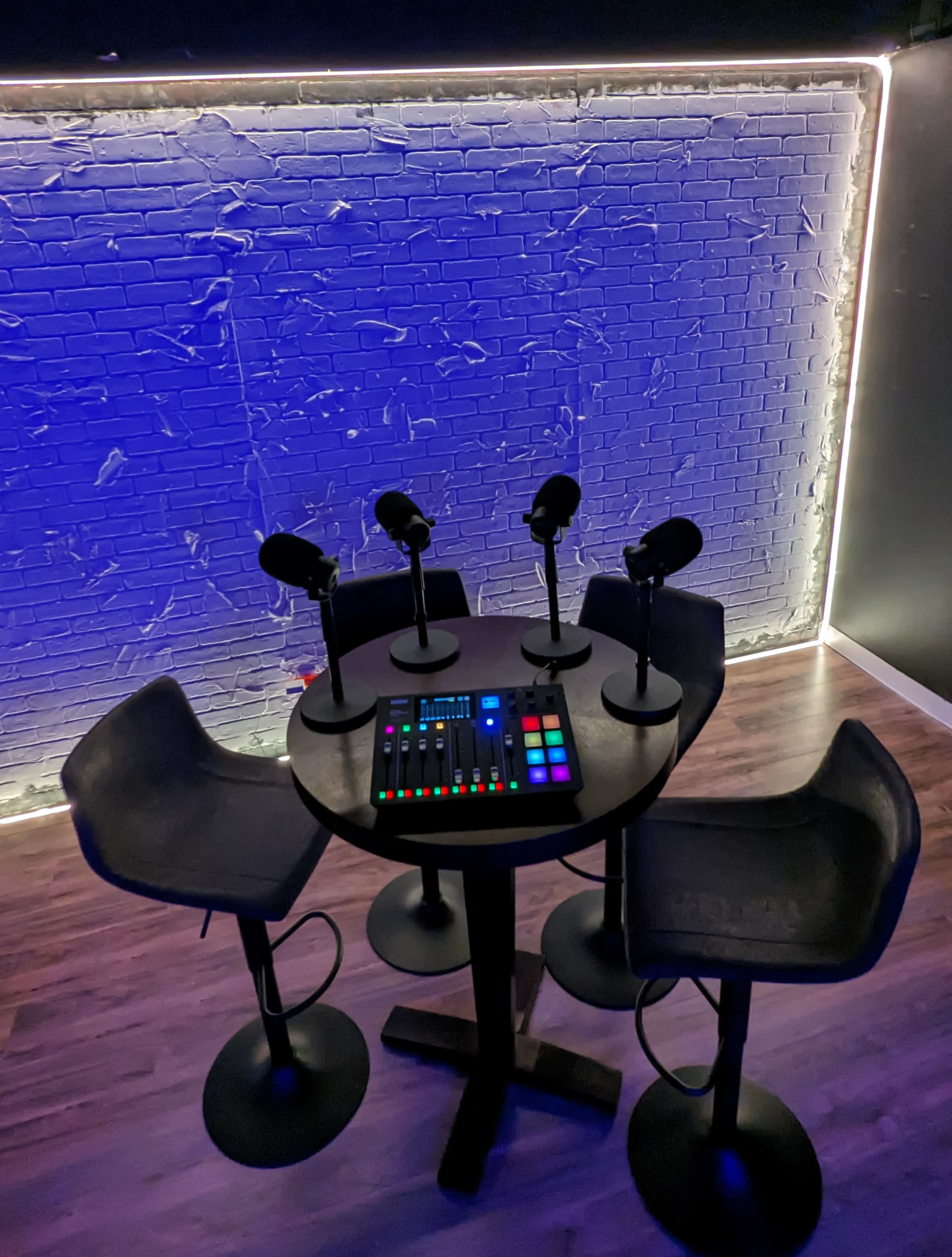 A small round table with four microphones and a control panel is set against a wall with blue lighting.