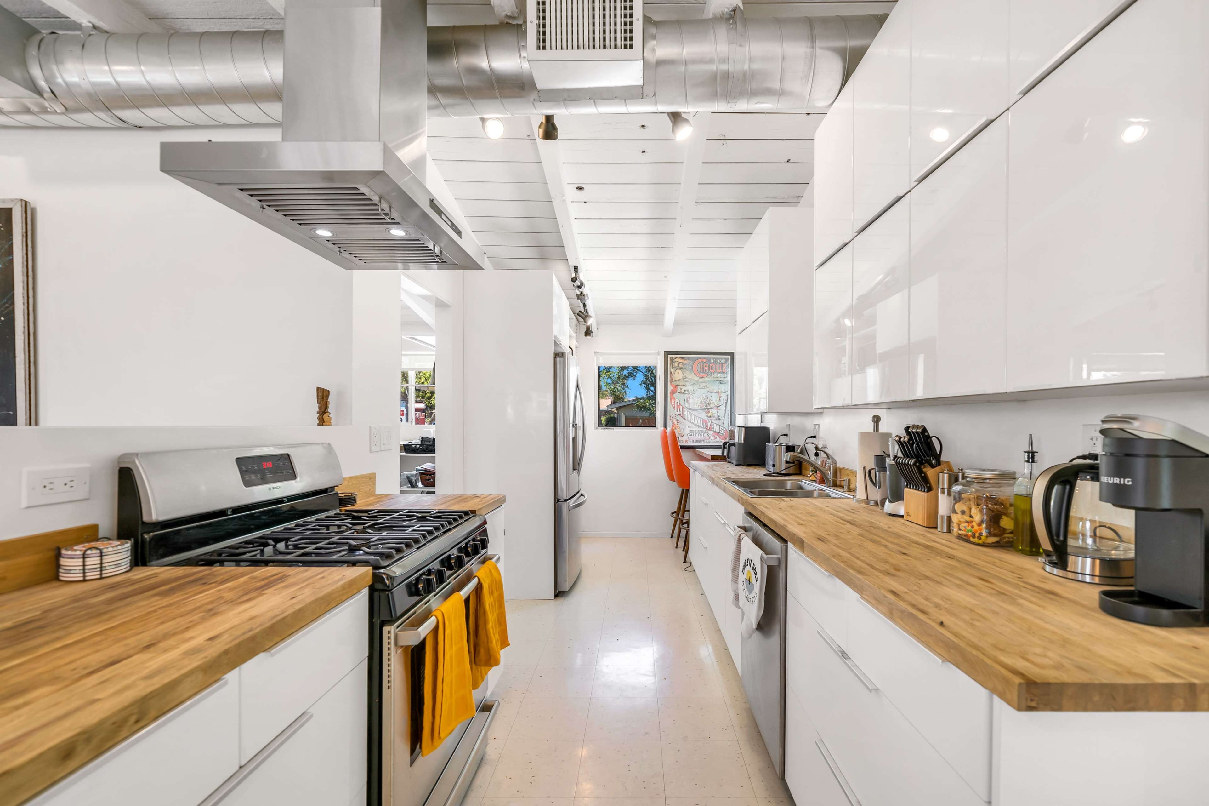 The image shows a modern kitchen with white cabinetry, stainless steel appliances, and wooden countertops.