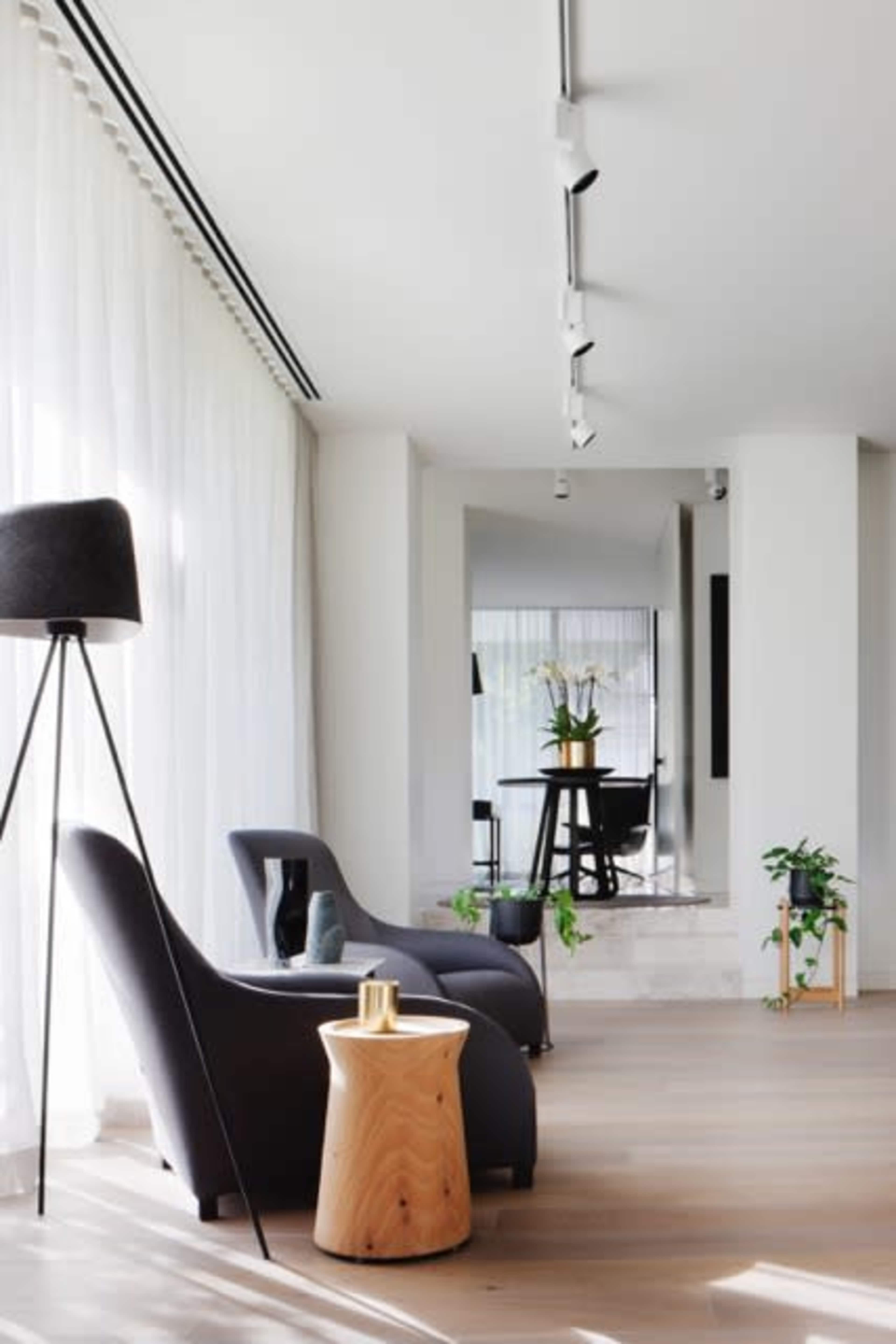 The image features a modern living area with two gray chairs, a wooden side table, and a floor lamp, complemented by large windows and plants.
