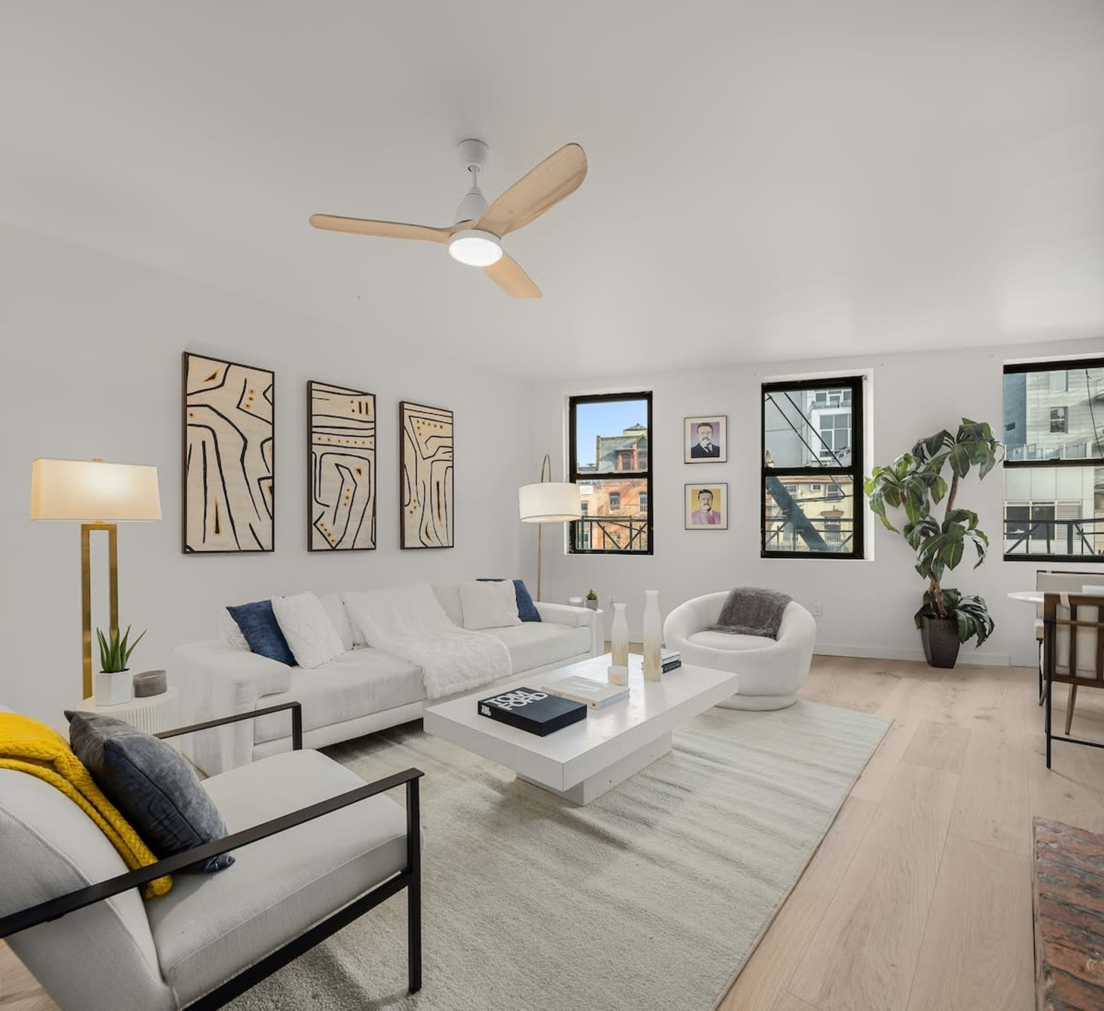 A spacious living room features a light color palette, modern furniture, and large windows illuminating the space.