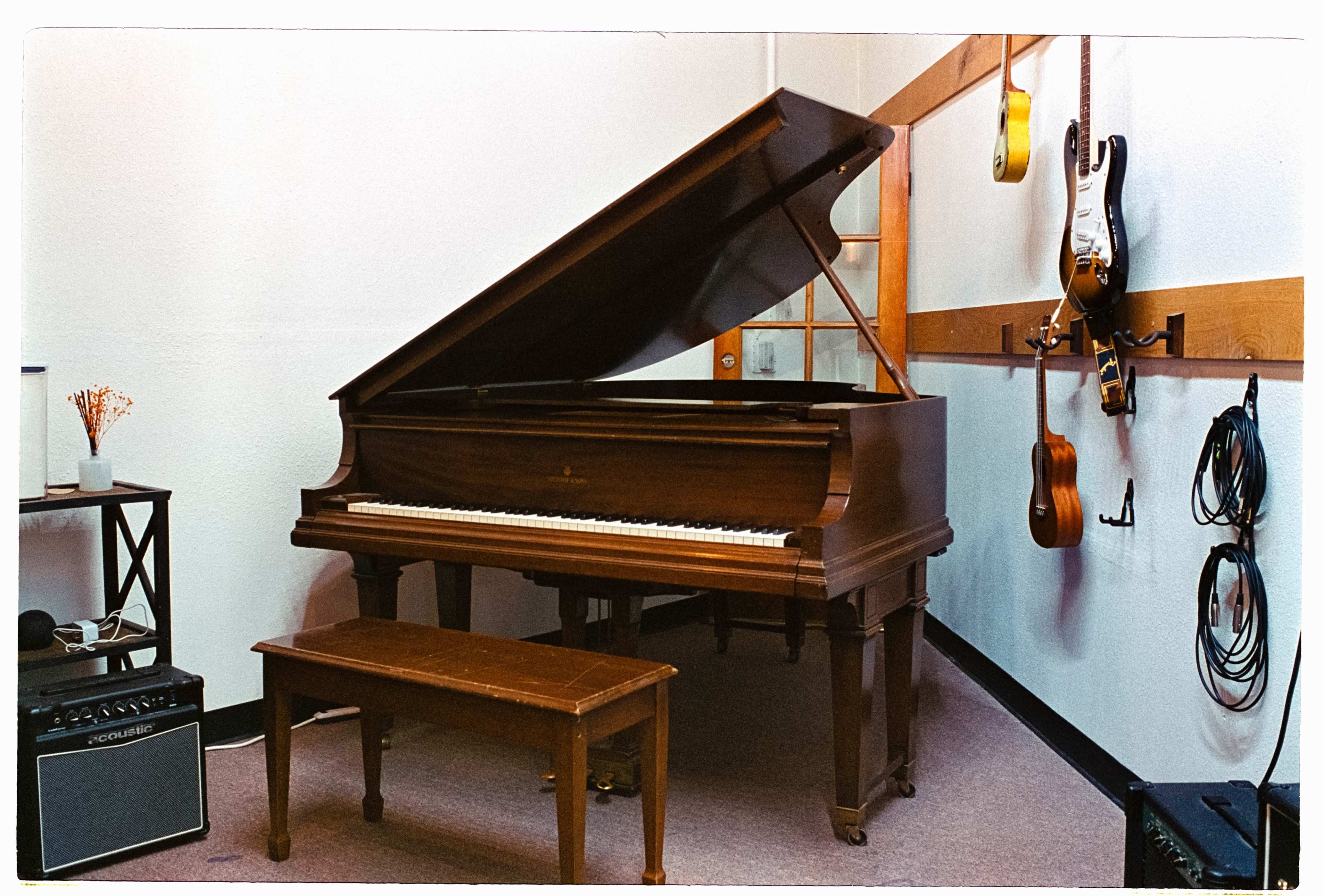 The image features a grand piano positioned in a cozy music room, accompanied by a small bench and various musical instruments hanging on the wall.