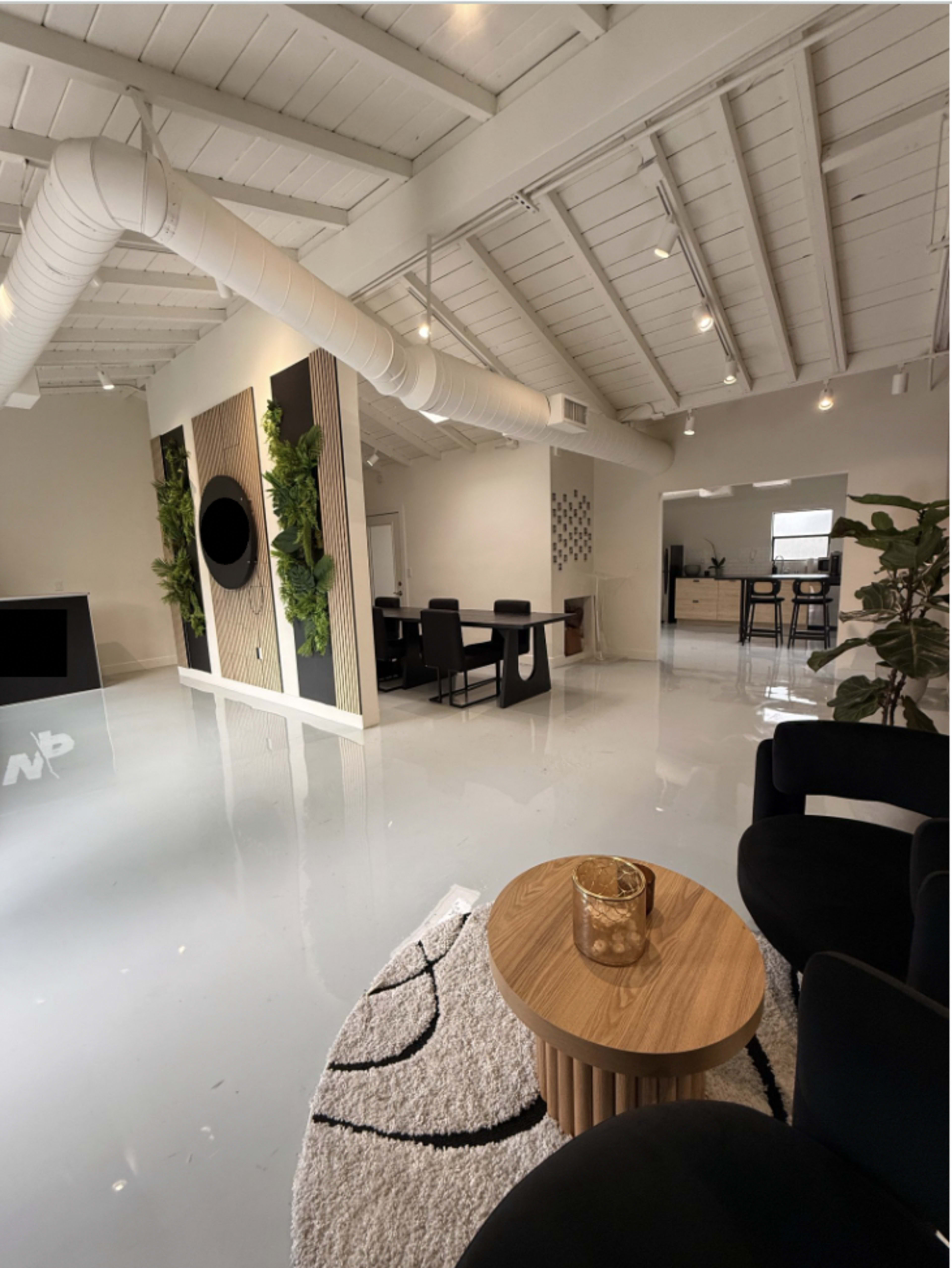 The image shows a modern office interior with a sleek design, featuring a reception area with a glass desk, seating arrangements, and plants along the walls.