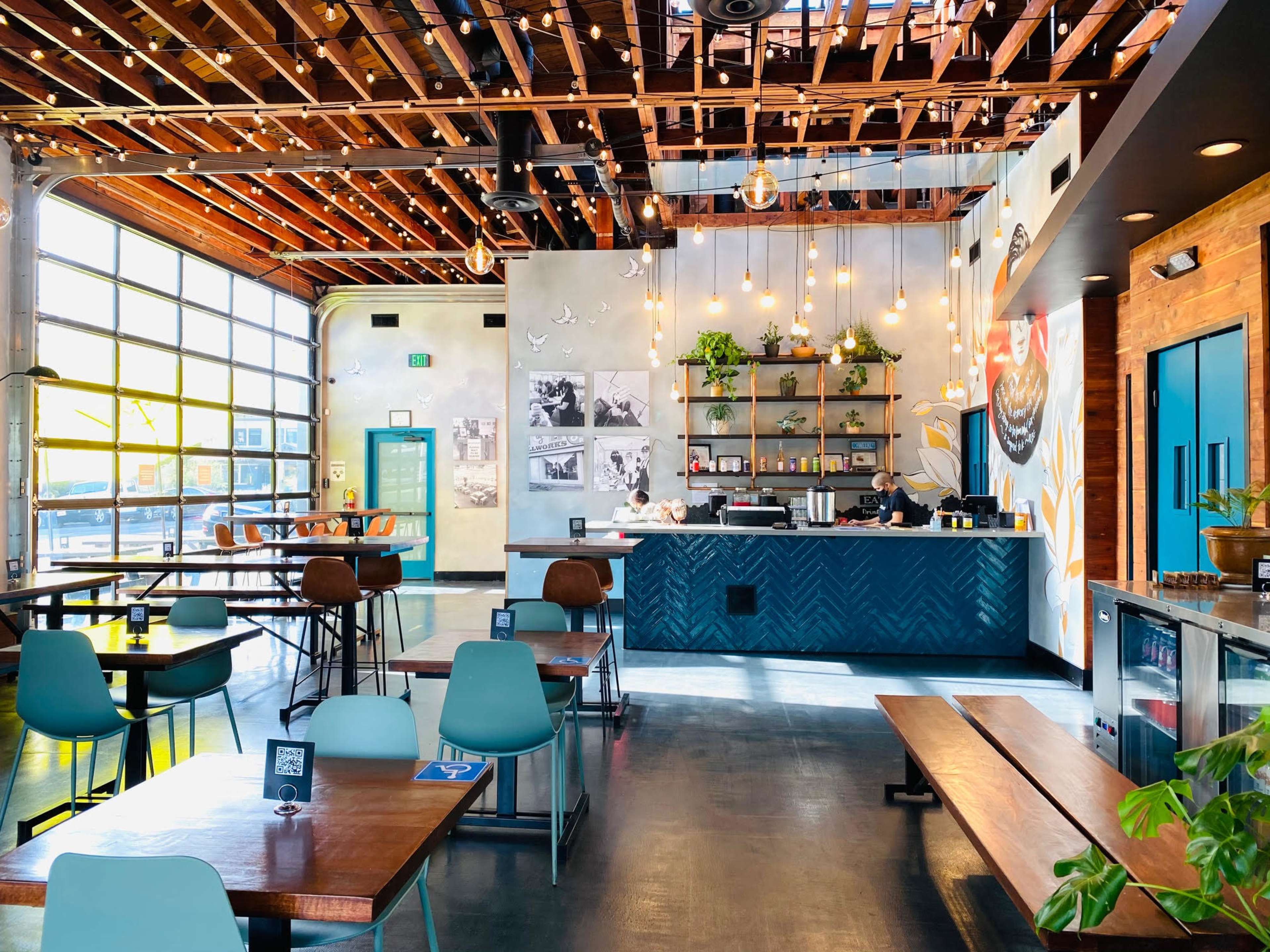 The interior of a modern restaurant features wooden beams, eclectic seating, and a service counter adorned with shelves and decor.