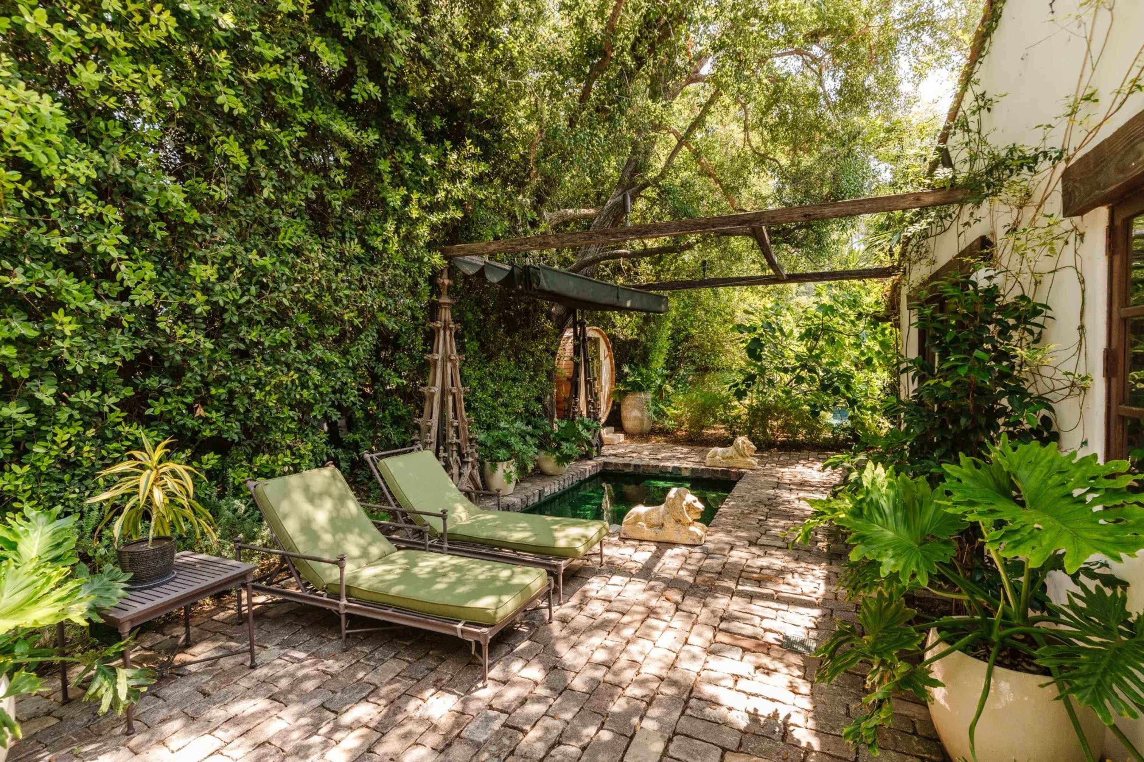 A secluded outdoor area features two green lounge chairs beside a narrow pool, surrounded by lush greenery and a stone patio.