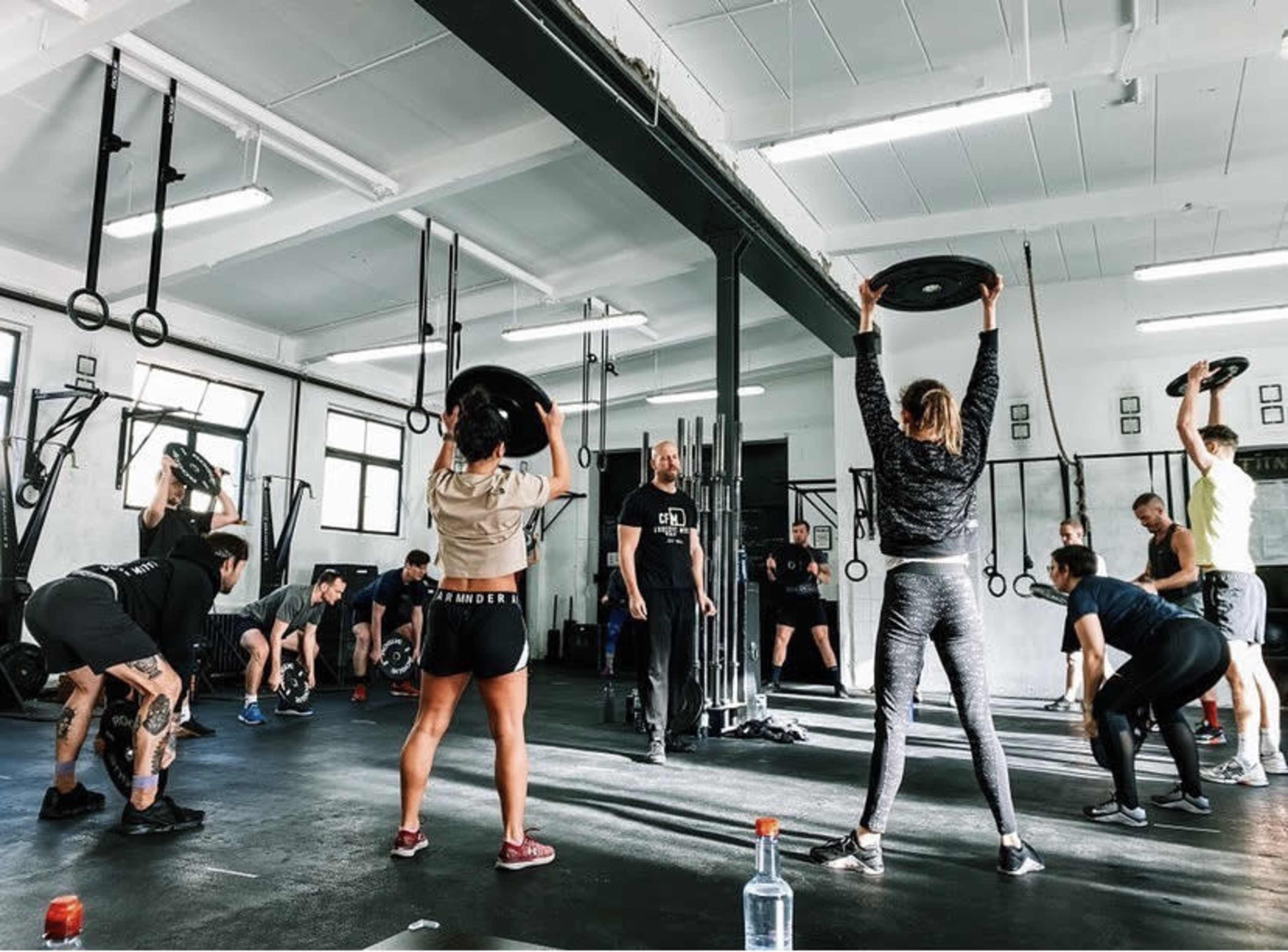 A group of people is engaged in a fitness class, lifting weights and following instructions in a well-equipped gym.