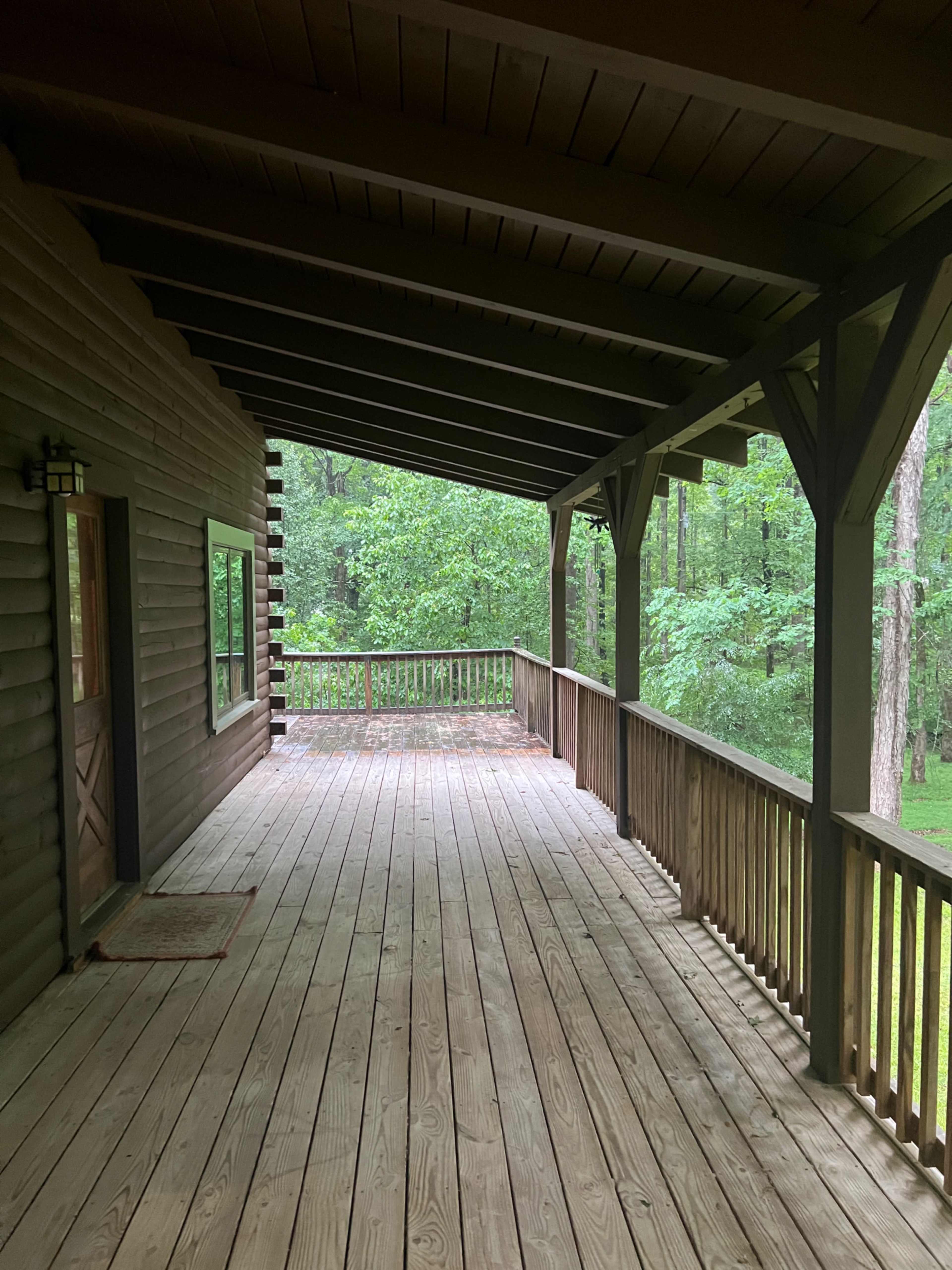 The image shows a wooden porch with a slatted floor and a roof, surrounded by a lush green forest.