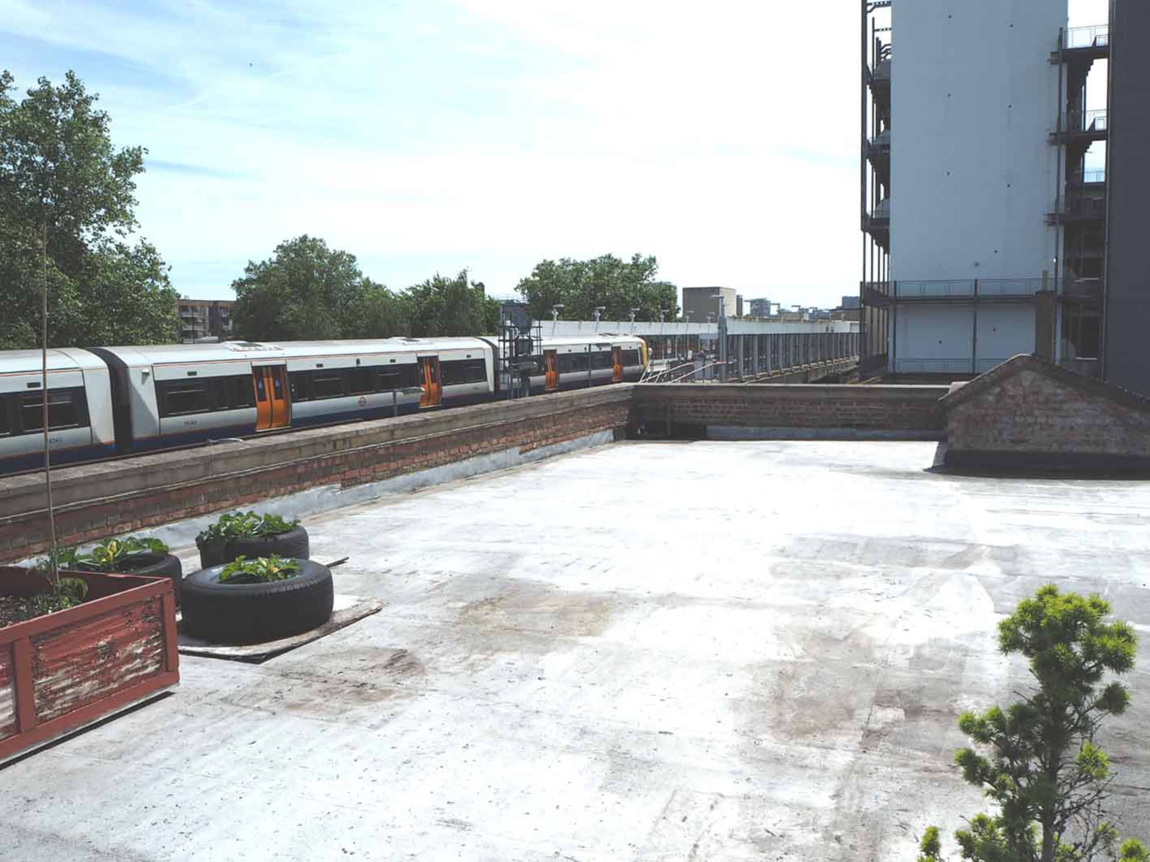 A train passes by on elevated tracks next to an empty rooftop garden area with planters and a nearby building under construction.
