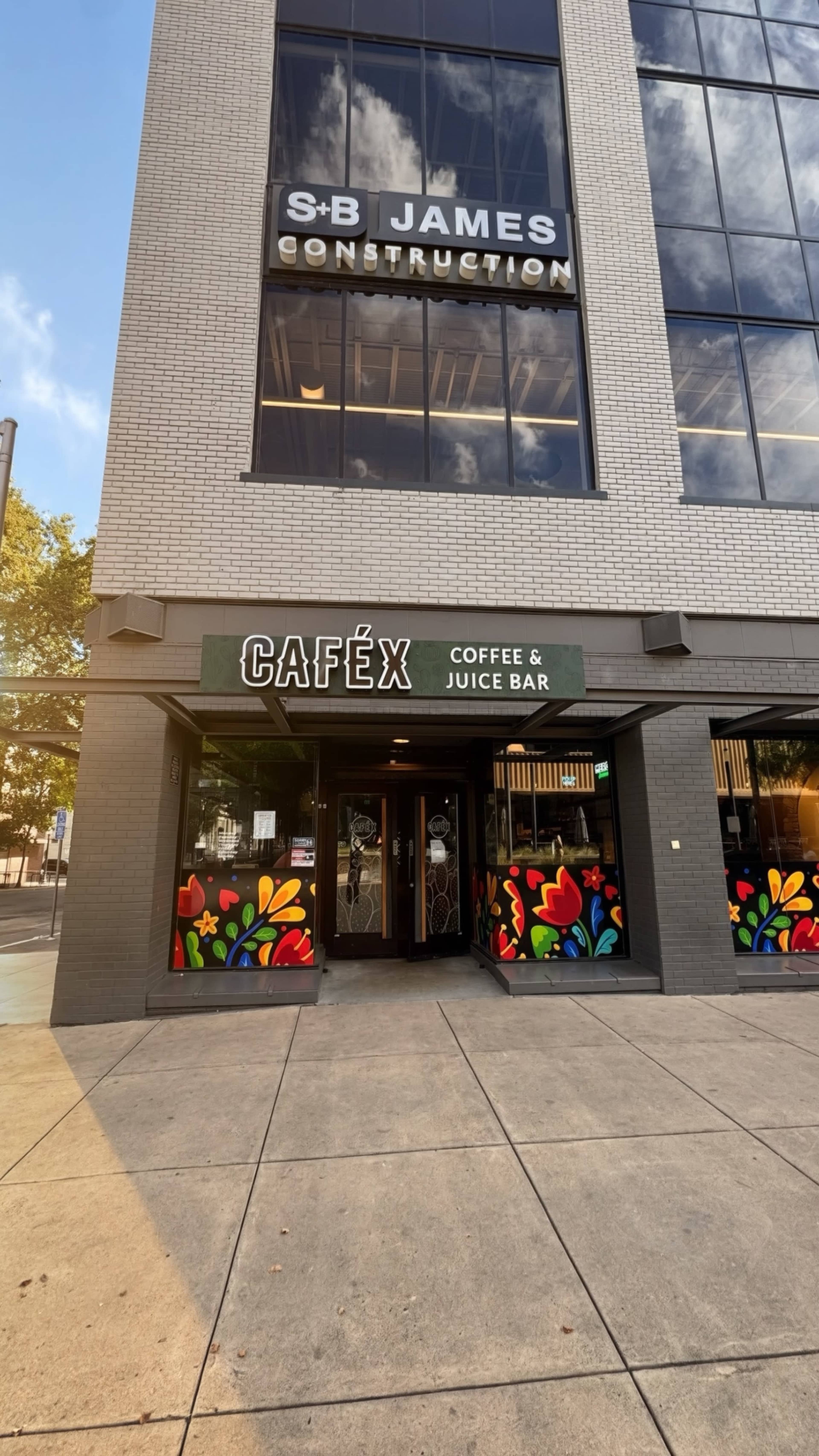 The image shows a modern building with a company name on the upper part and a colorful café entrance below, labeled "CAFÉX COFFEE & JUICE BAR."