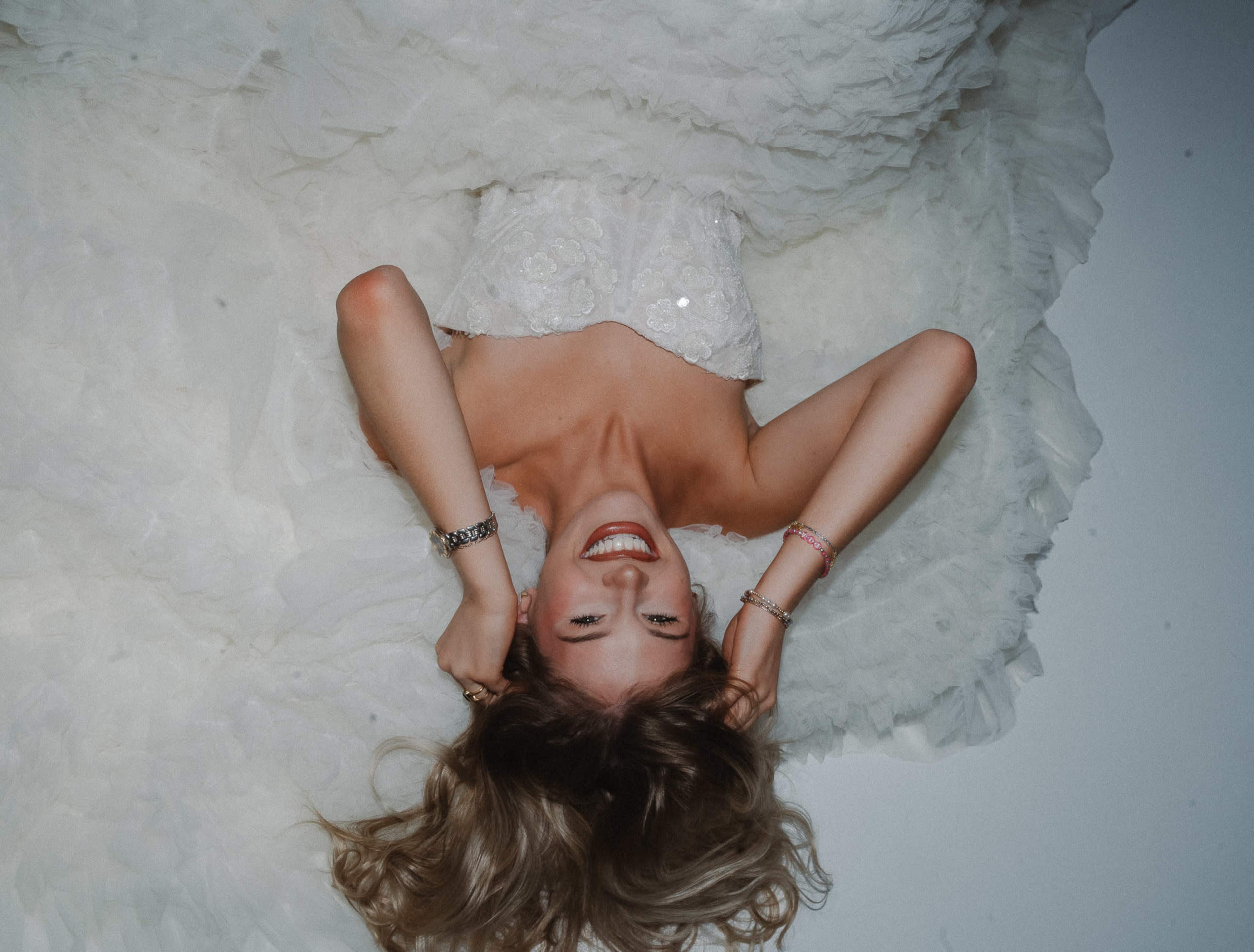 A bride in a white wedding dress lies on her back with her hair spread out around her.