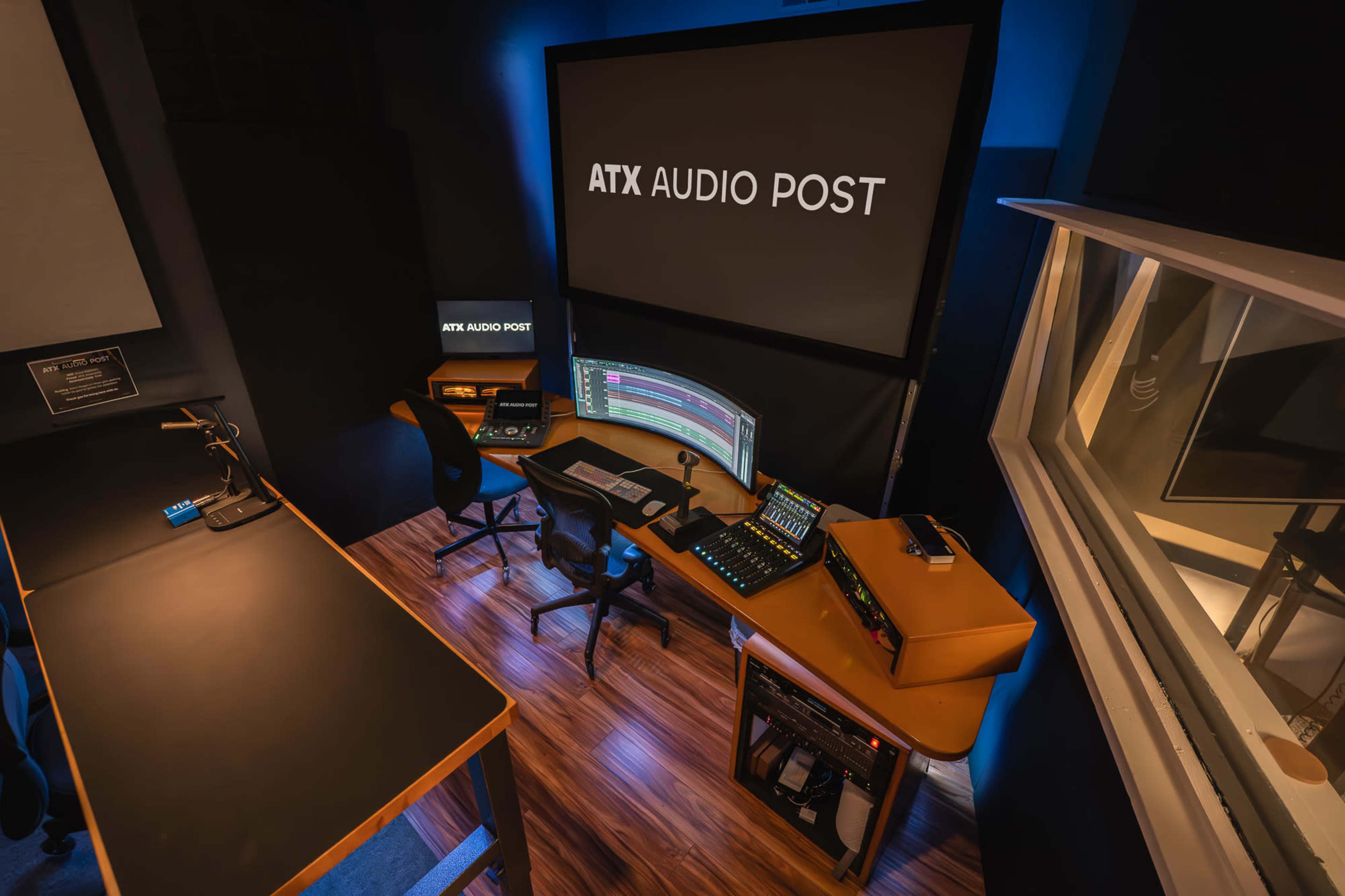 The image shows a sound editing studio equipped with a computer workstation, audio mixing equipment, and large screens displaying the studio name "ATX AUDIO POST."