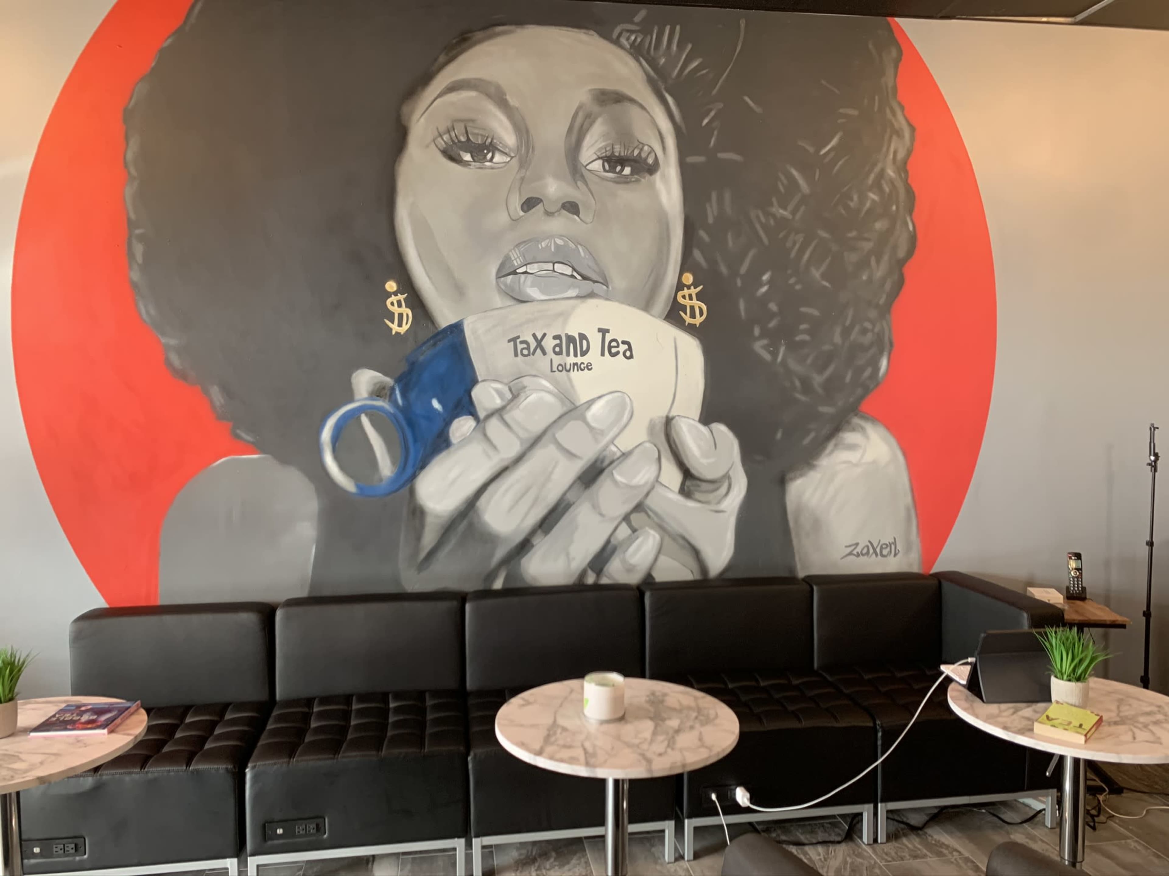 A mural of a woman holding a cup labeled "Tax and Tea" against a red background, with a modern seating area in front.