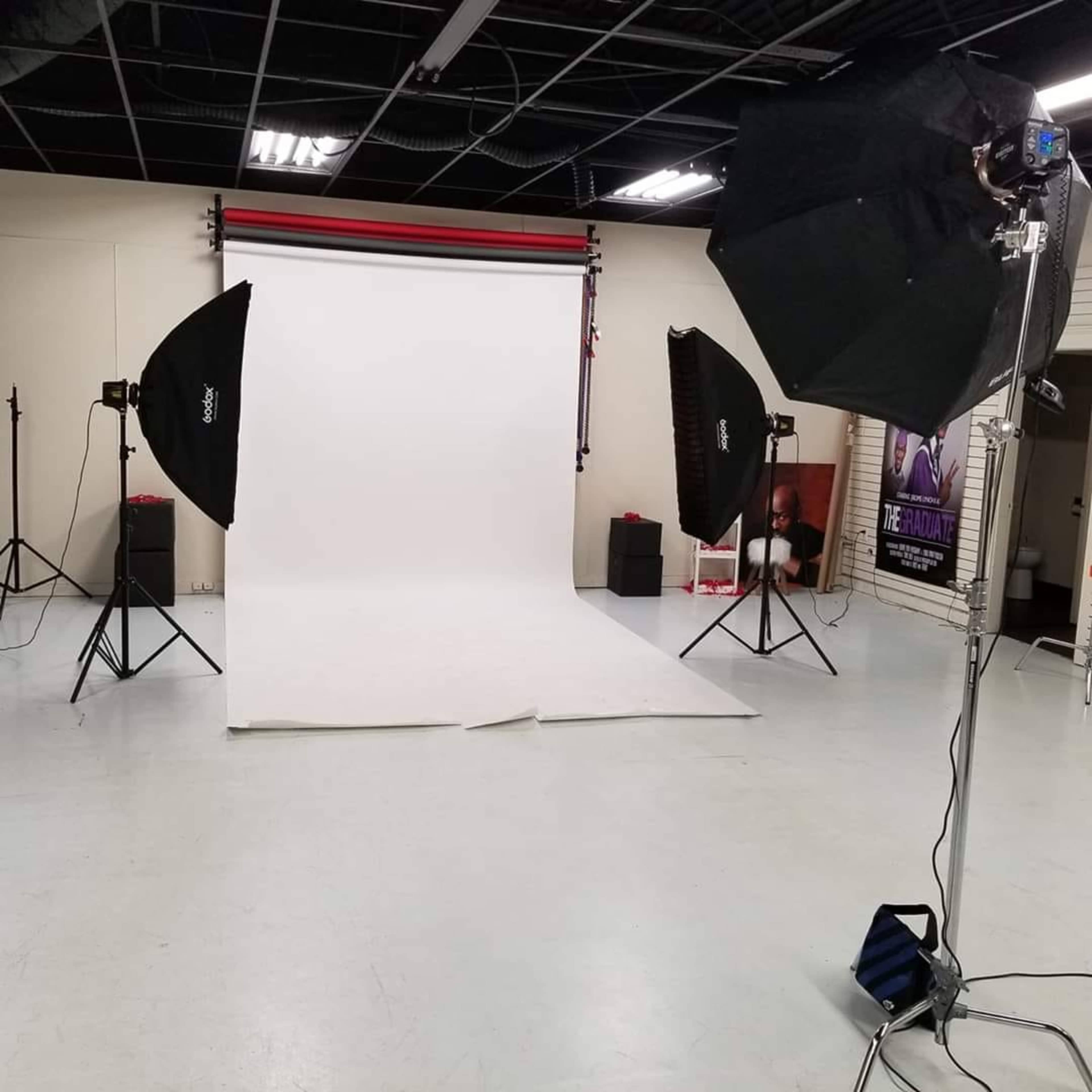 A photography studio is set up with a white backdrop, softbox lights, and various equipment arranged on the floor.