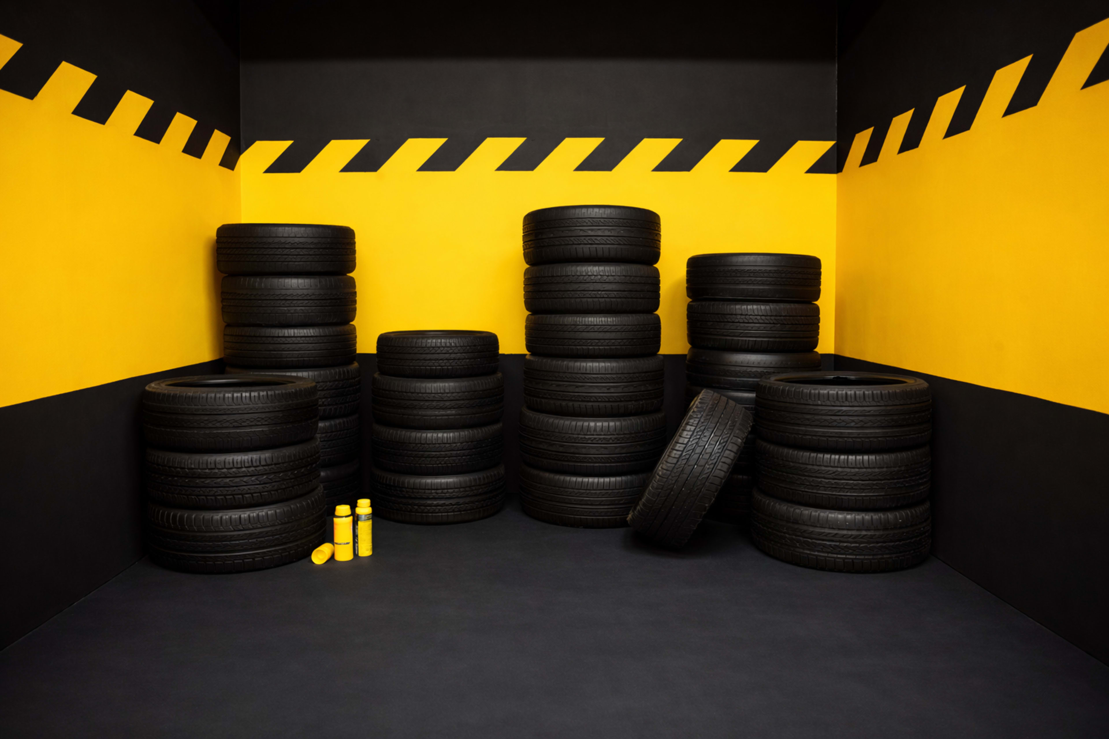The image shows a collection of black tires stacked in a corner of a room with yellow and black striped walls.