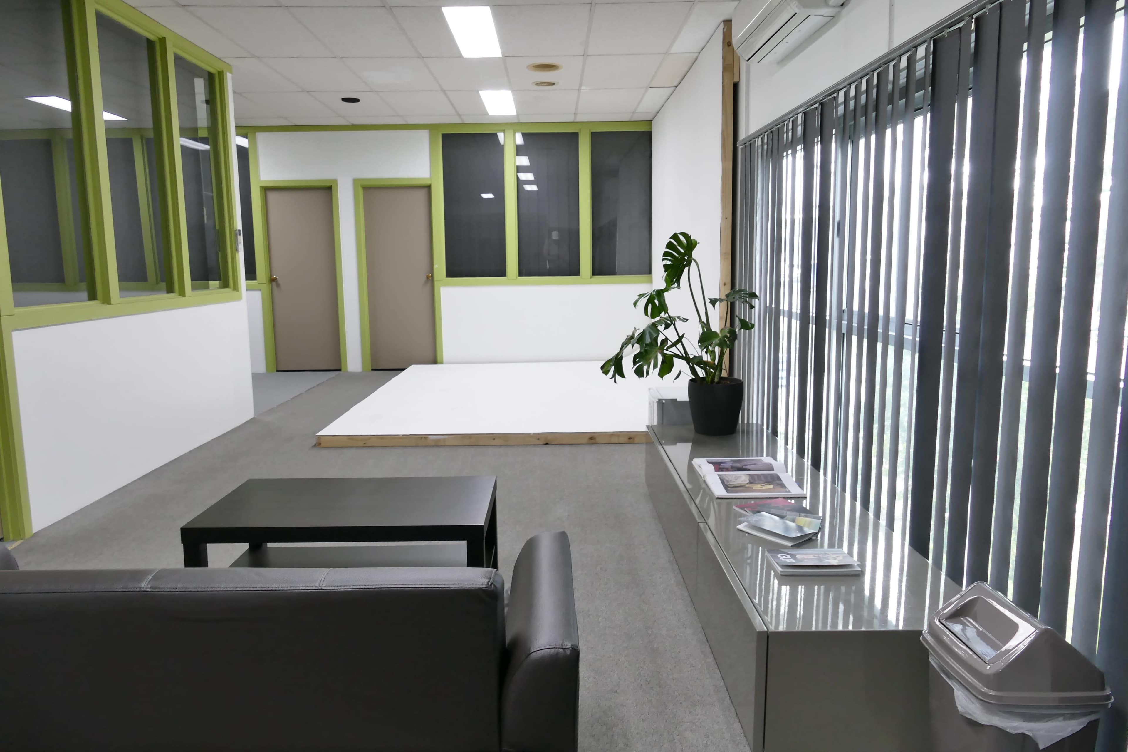 A modern workspace with a gray sofa, a glass table displaying magazines, and green-accented walls.