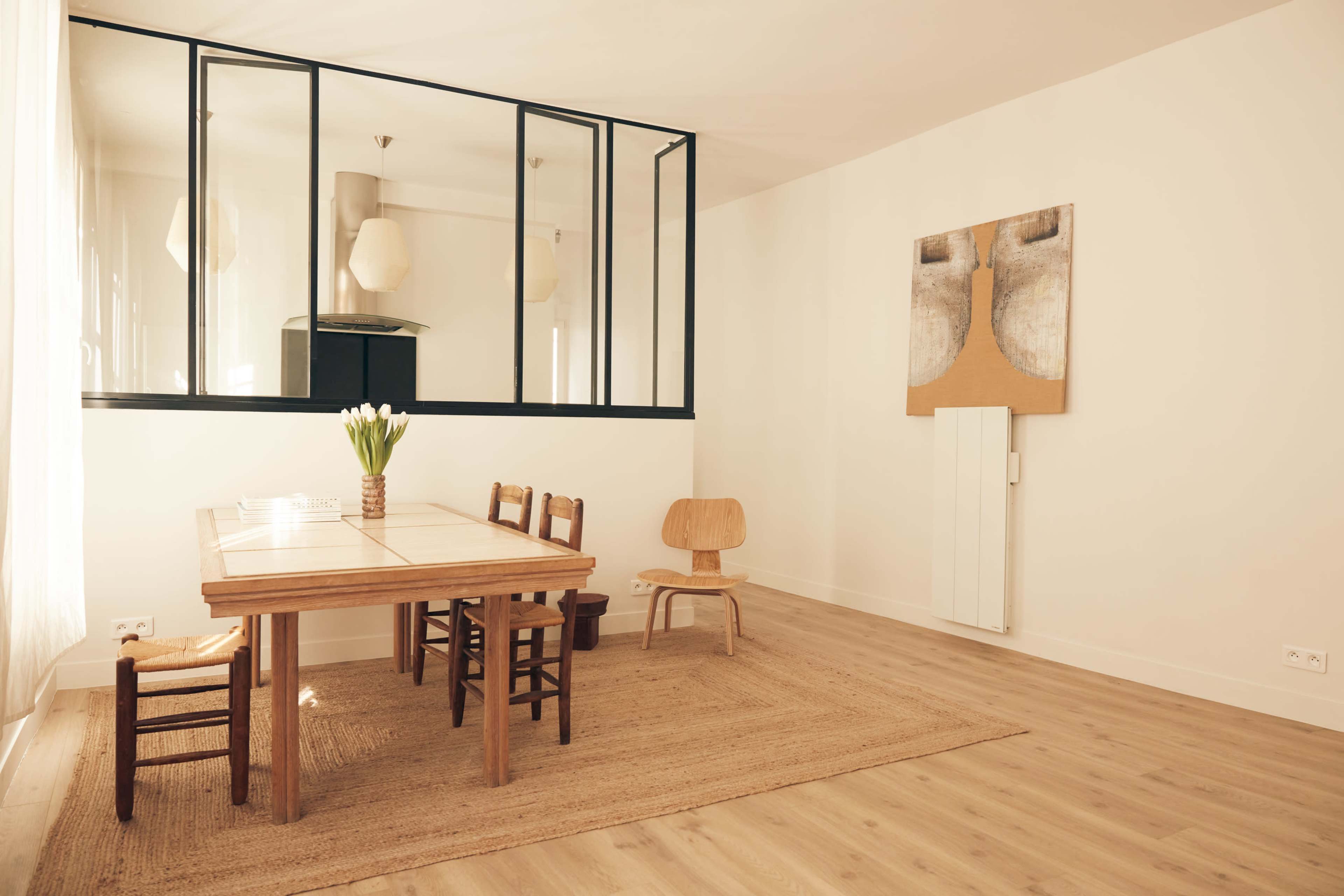 A modern dining area featuring a wooden table surrounded by four chairs, with a minimalist design and a large wall art piece.