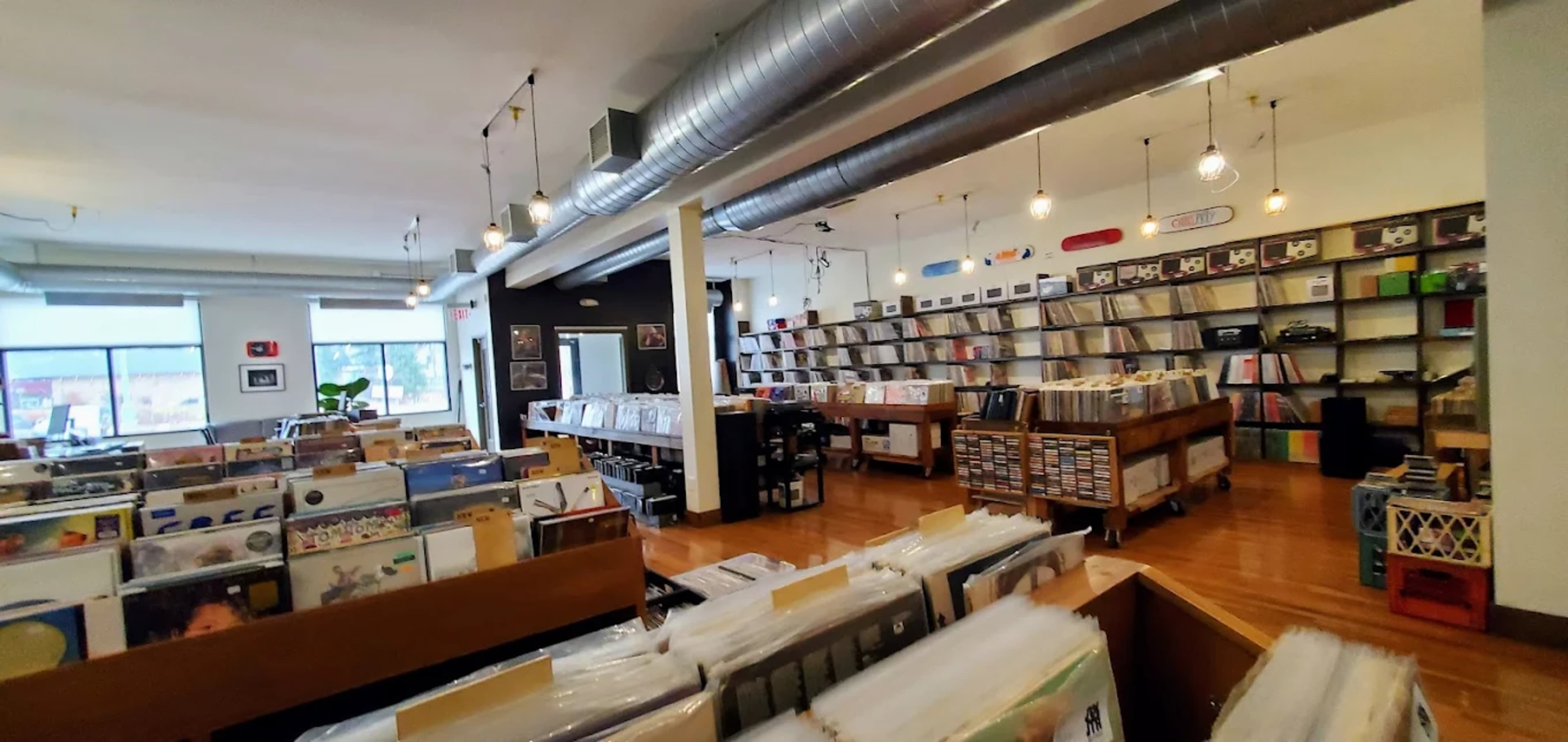 The image shows an interior of a vinyl record store with rows of records displayed on shelves and wooden bins.