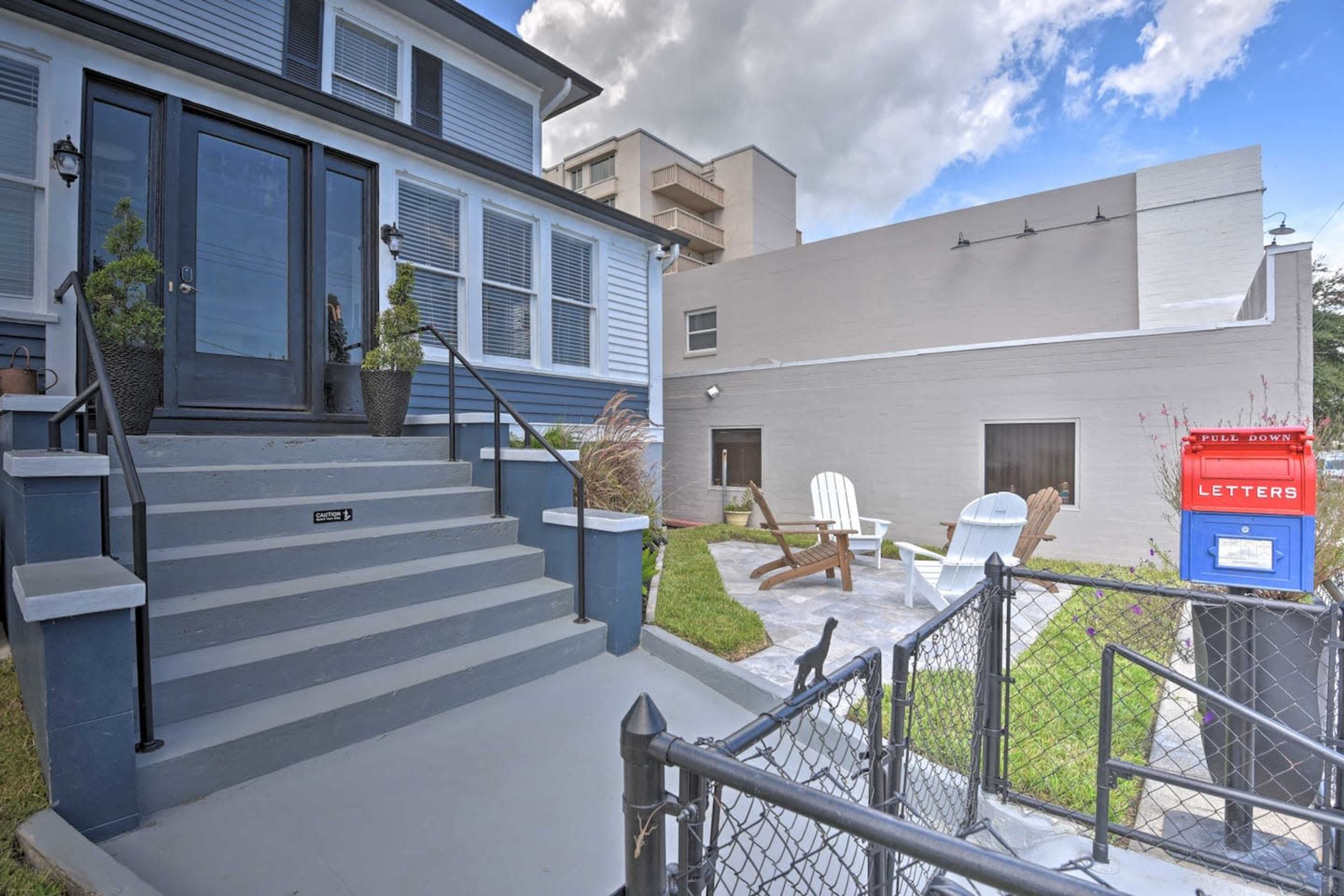A blue and gray house features a front entrance with stairs and a fence, alongside a red mailbox and a small outdoor seating area.