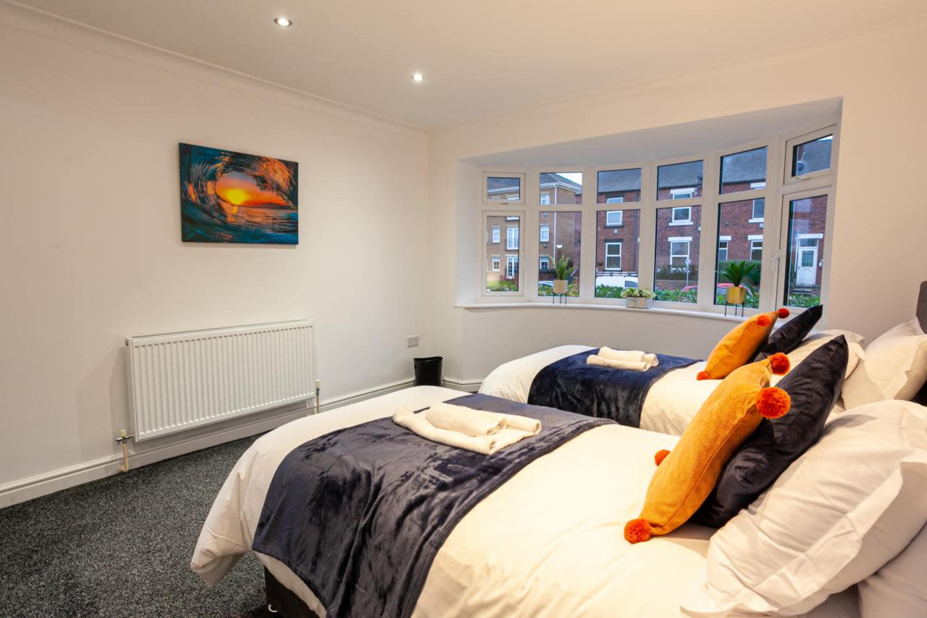 A well-lit bedroom with two single beds, each adorned with pillows and towels, and a large bay window overlooking a garden.