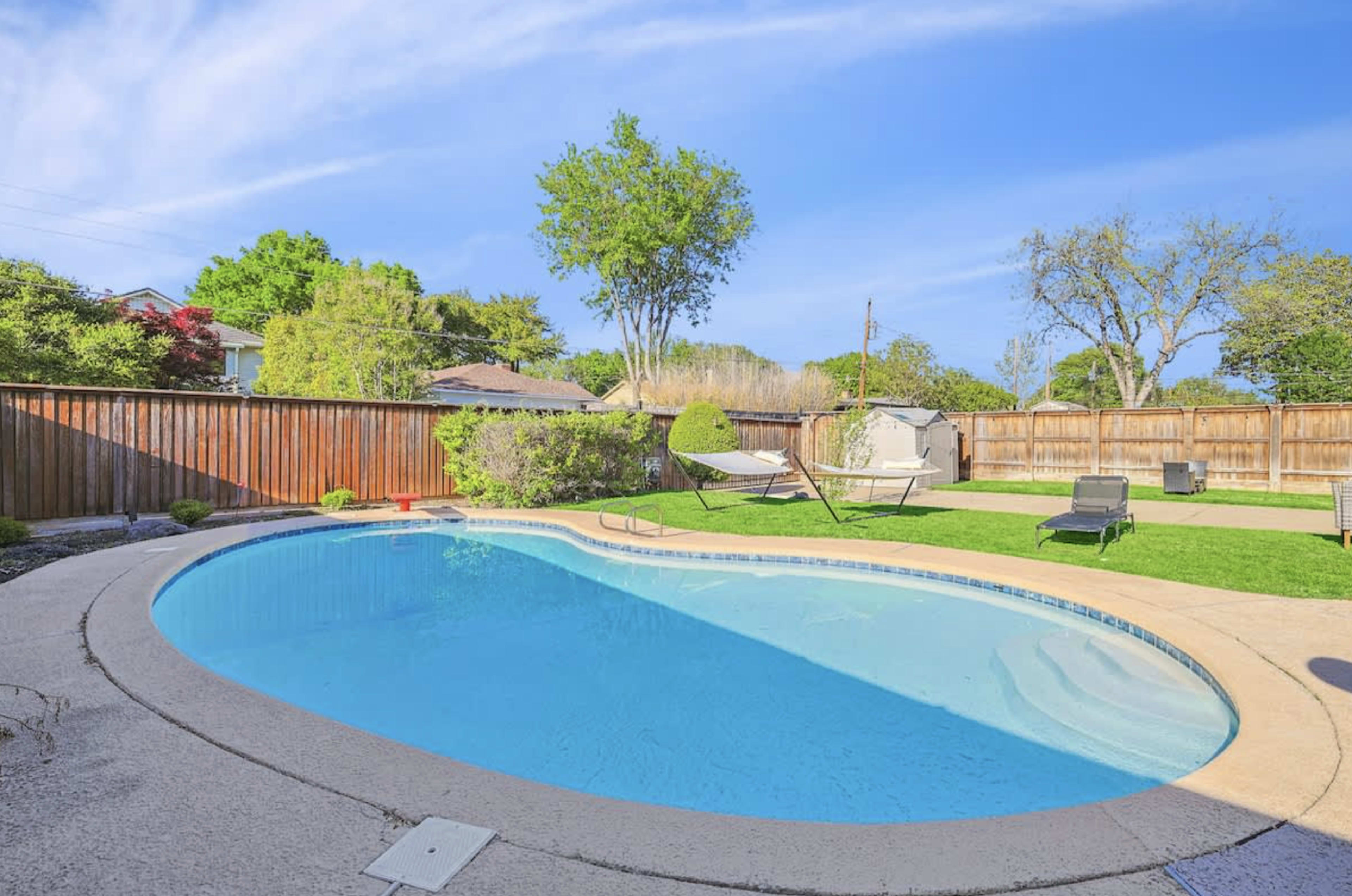The image shows a backyard with a swimming pool, two hammocks, and a fenced area with trees and green grass.