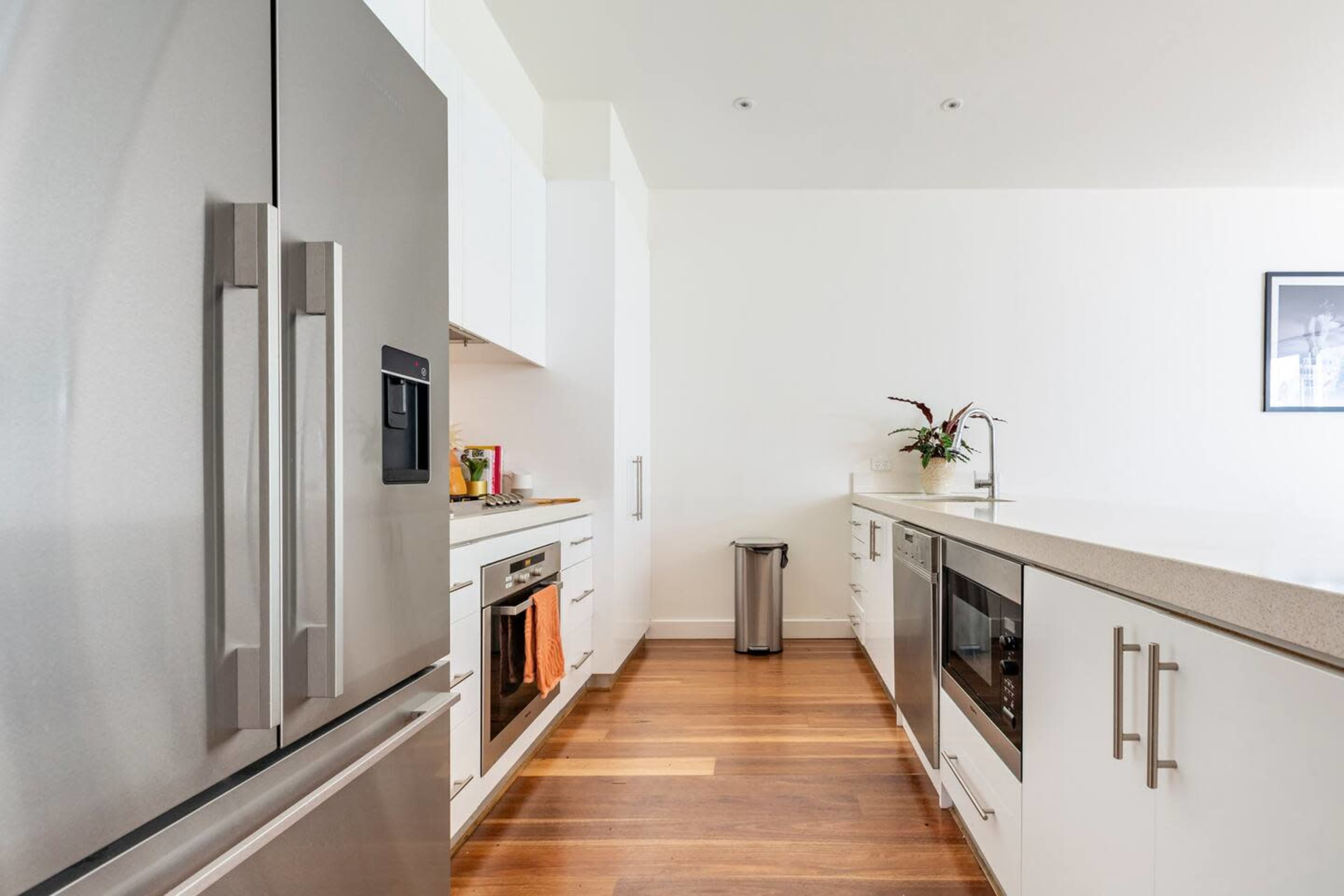 A modern kitchen features stainless steel appliances, wooden flooring, and white cabinetry.