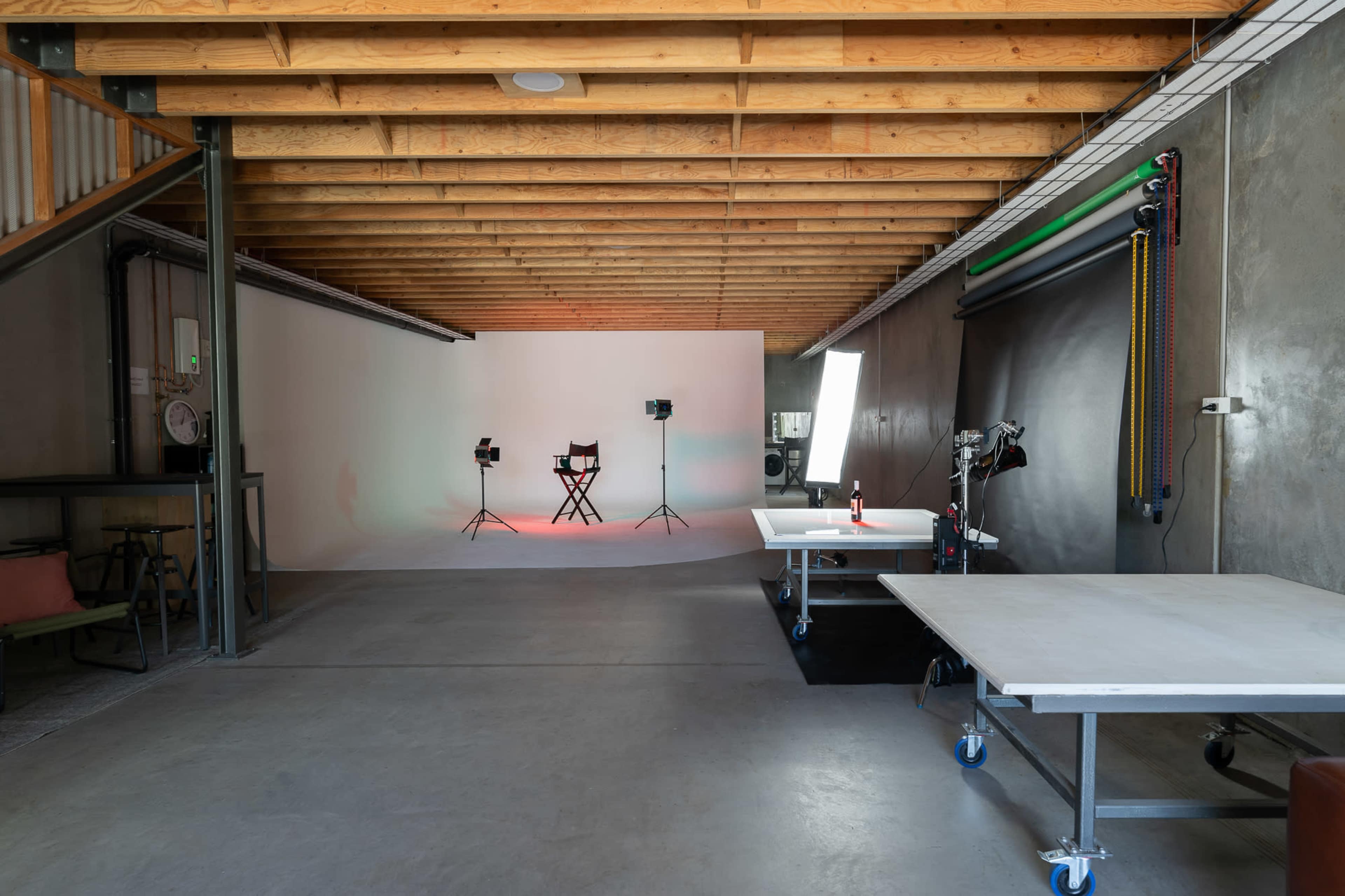 A photography studio with a minimalist design, featuring a blank backdrop, lights, a director's chair, and work tables.