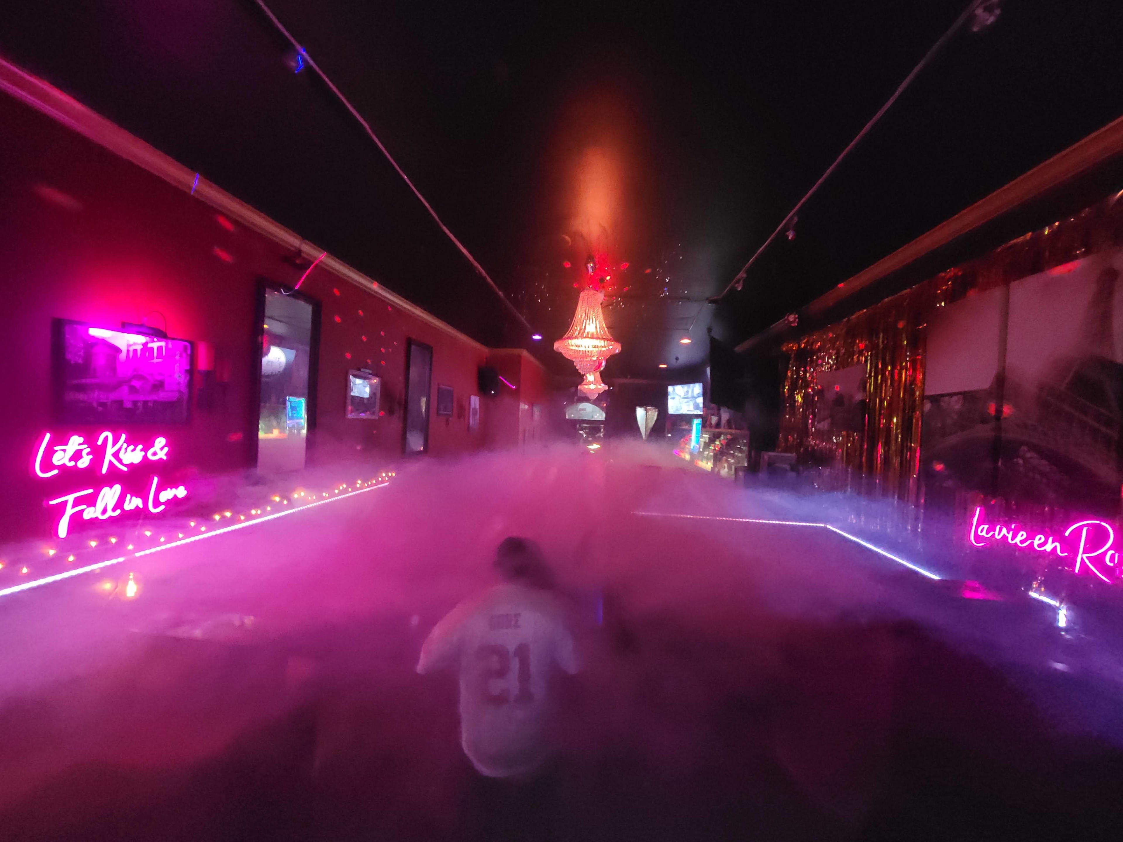 A dimly lit room with colorful neon signs, a chandelier, and a foggy atmosphere.