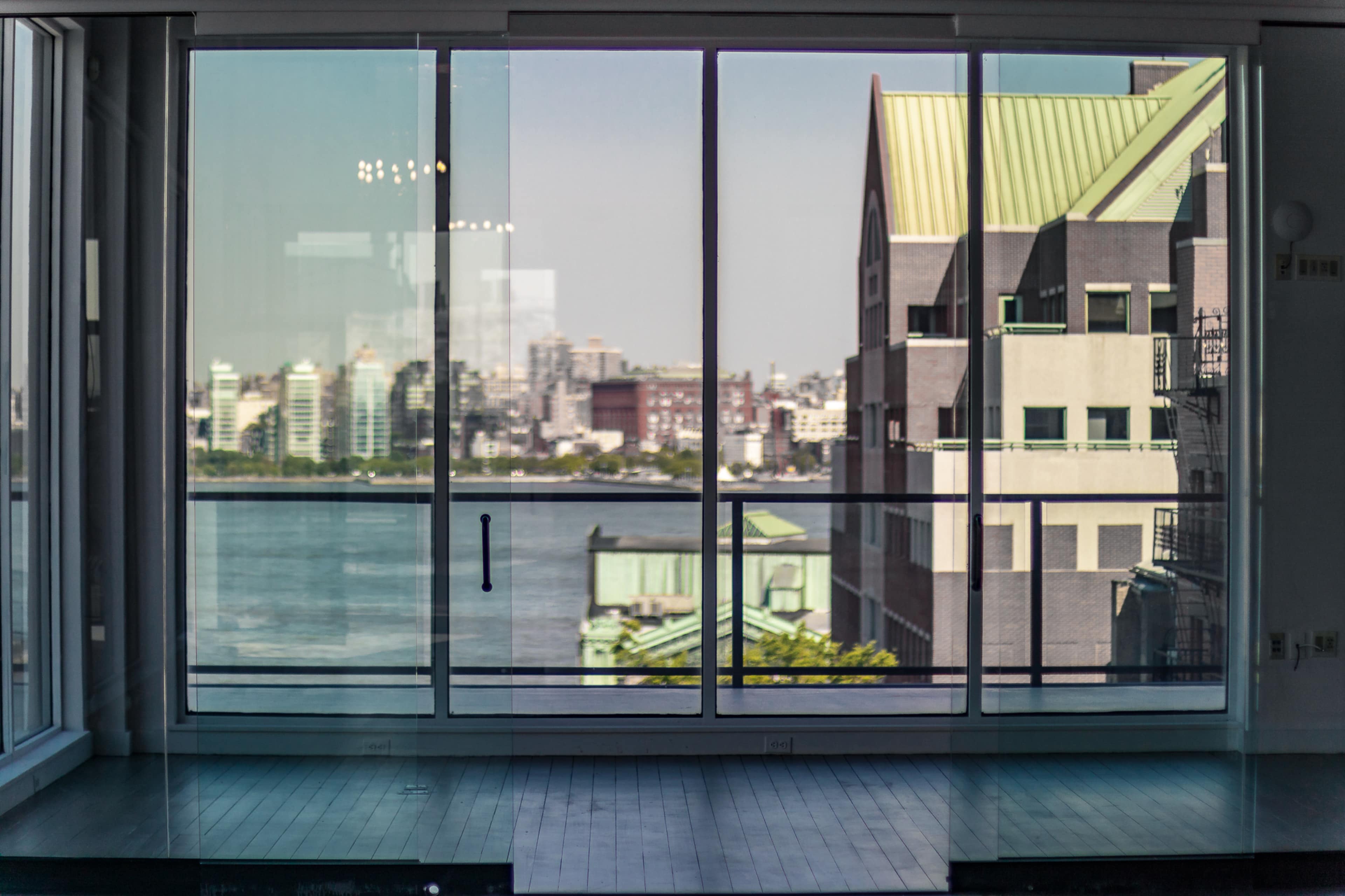 A large glass sliding door opening to a view of a body of water and modern buildings across the shore.
