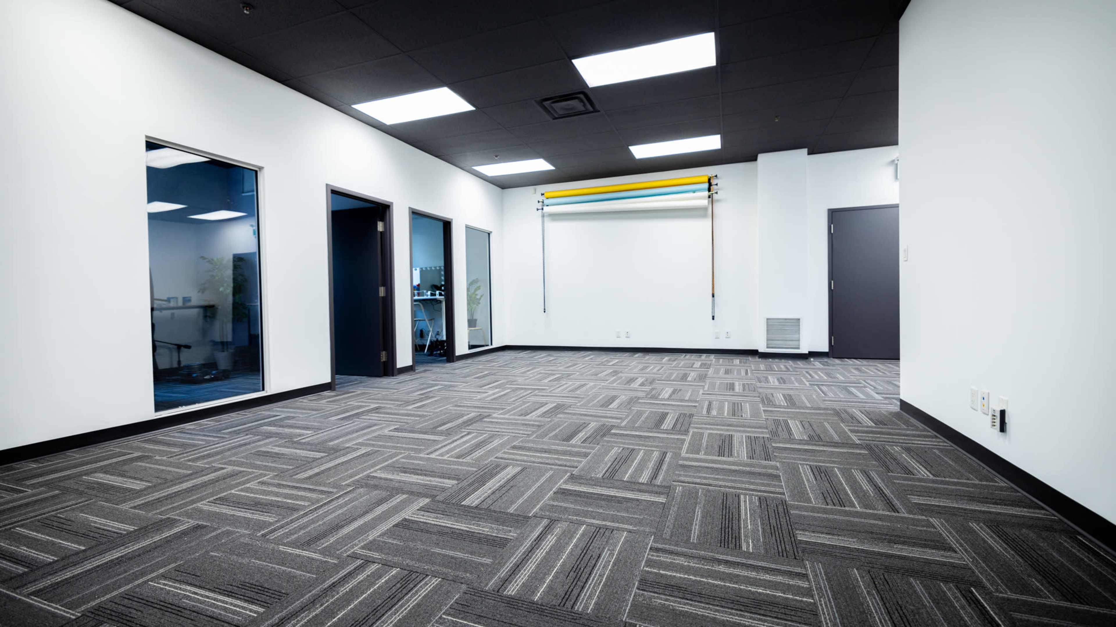 A spacious empty office room with patterned carpet, white walls, and three doorways leading to adjacent rooms.