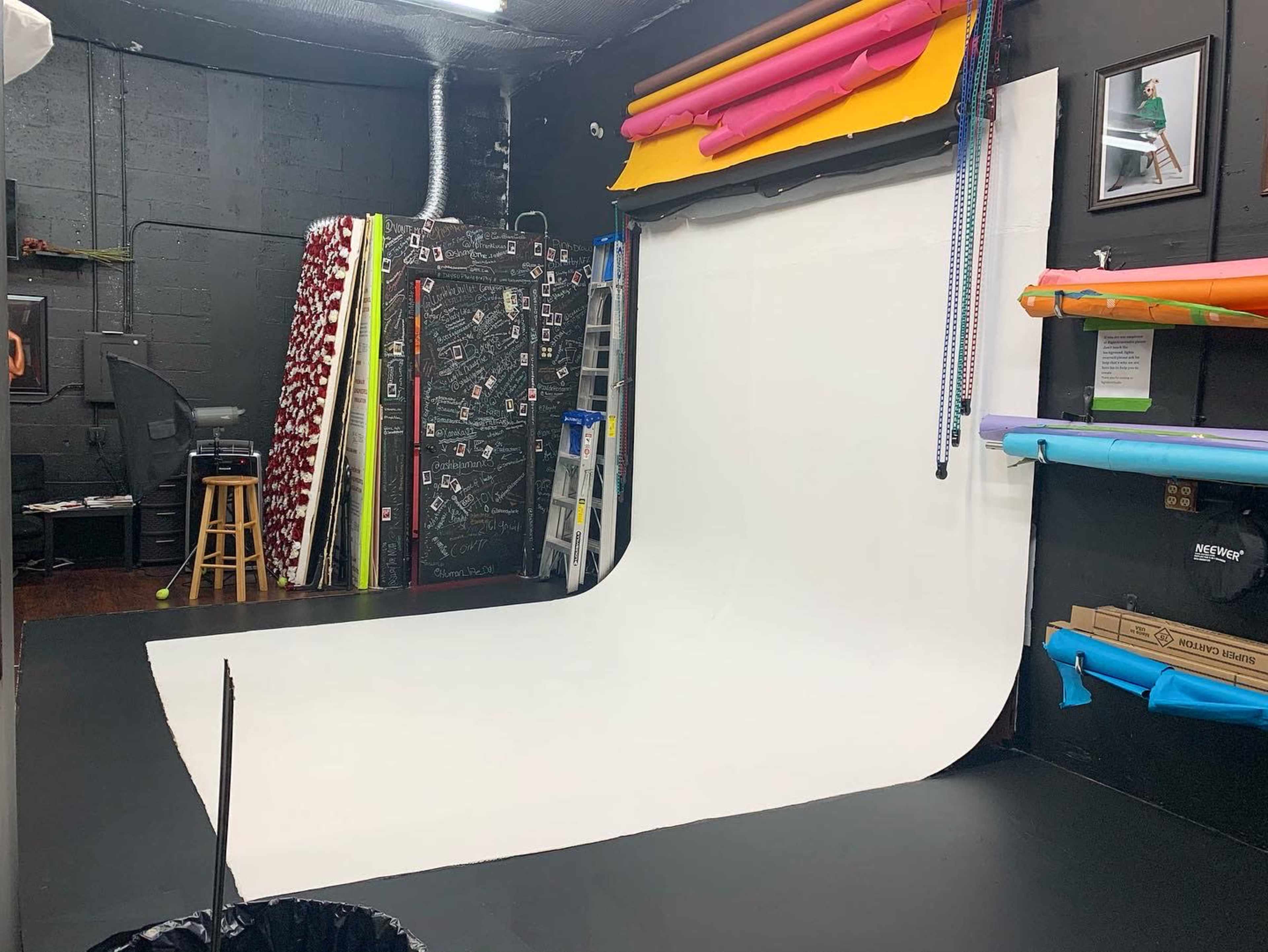 A photography studio with a white backdrop, colorful backdrop rolls on the walls, and a ladder in the corner.